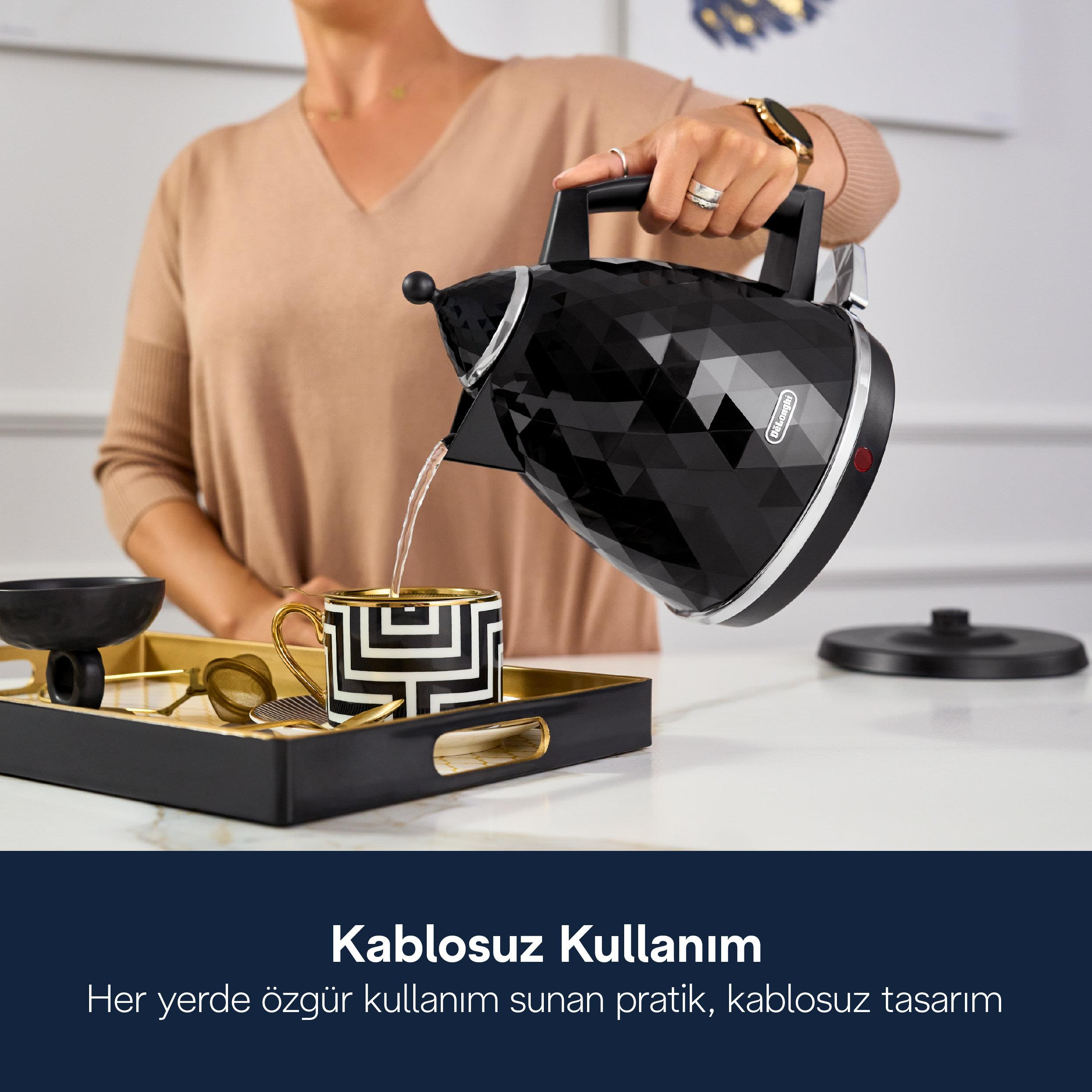 Kobieta nalewa wodę z czajnika do ozdobnego kubka na tacy.