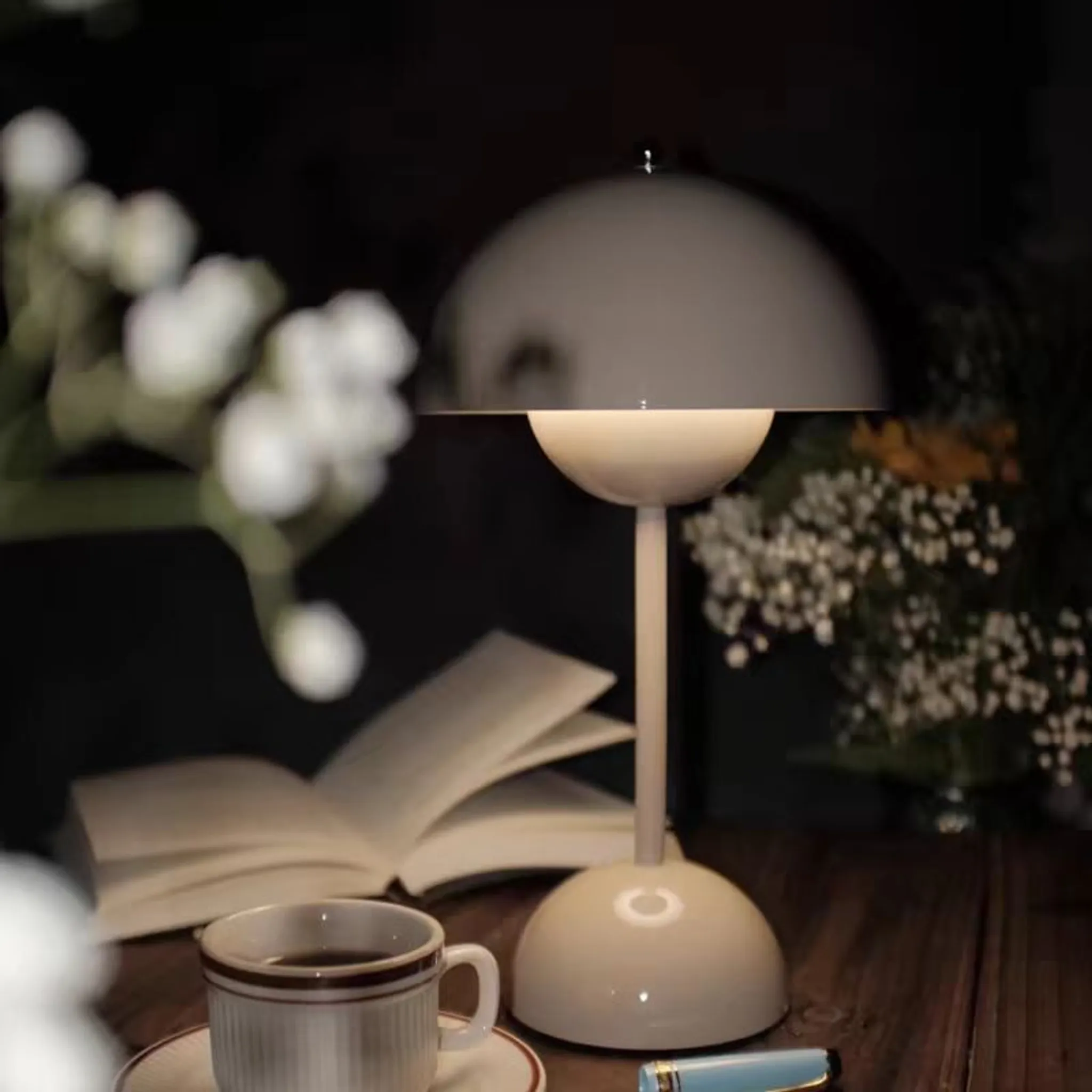 Eine Lampe beleuchtet ein offenes Buch, eine Kaffeetasse und eine Feder auf einem Holztisch.