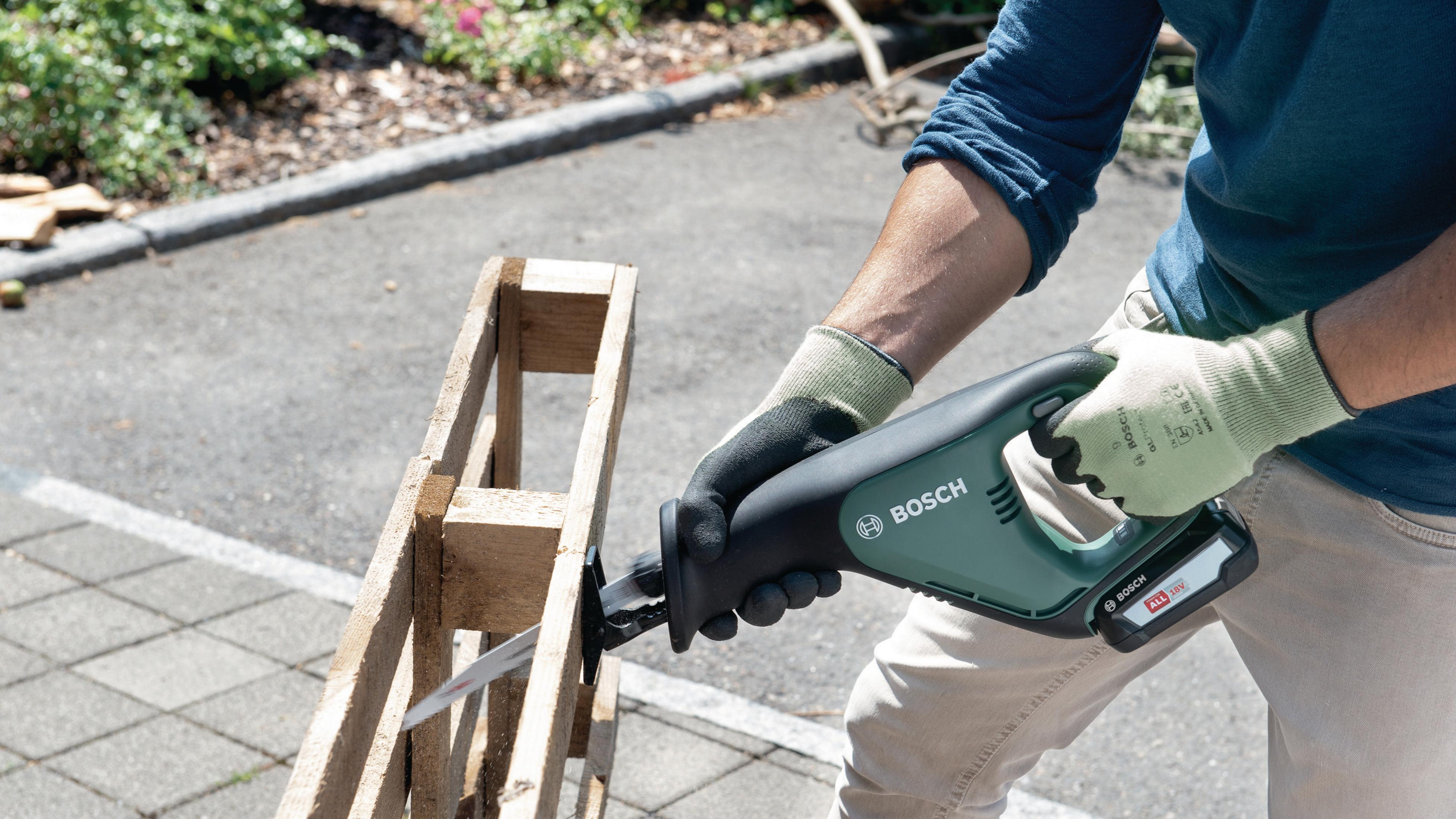 Eine Person zerlegt eine Holzpalette mit einem Säbelsäge-Werkzeug.