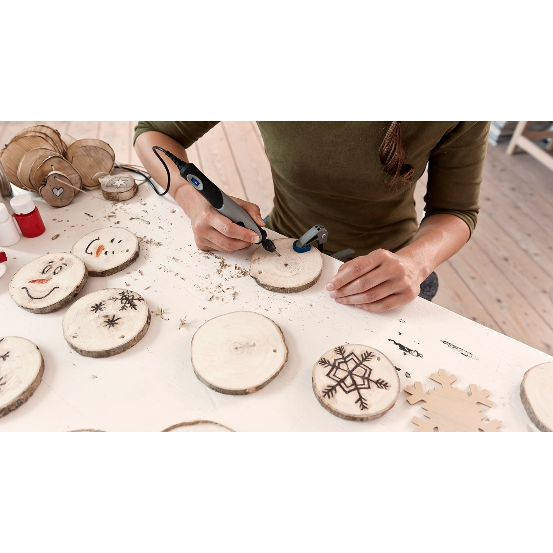 Eine Person bearbeitet Holzscheiben mit einem Dremel-Werkzeug, einige mit Schneemann-Motiven.