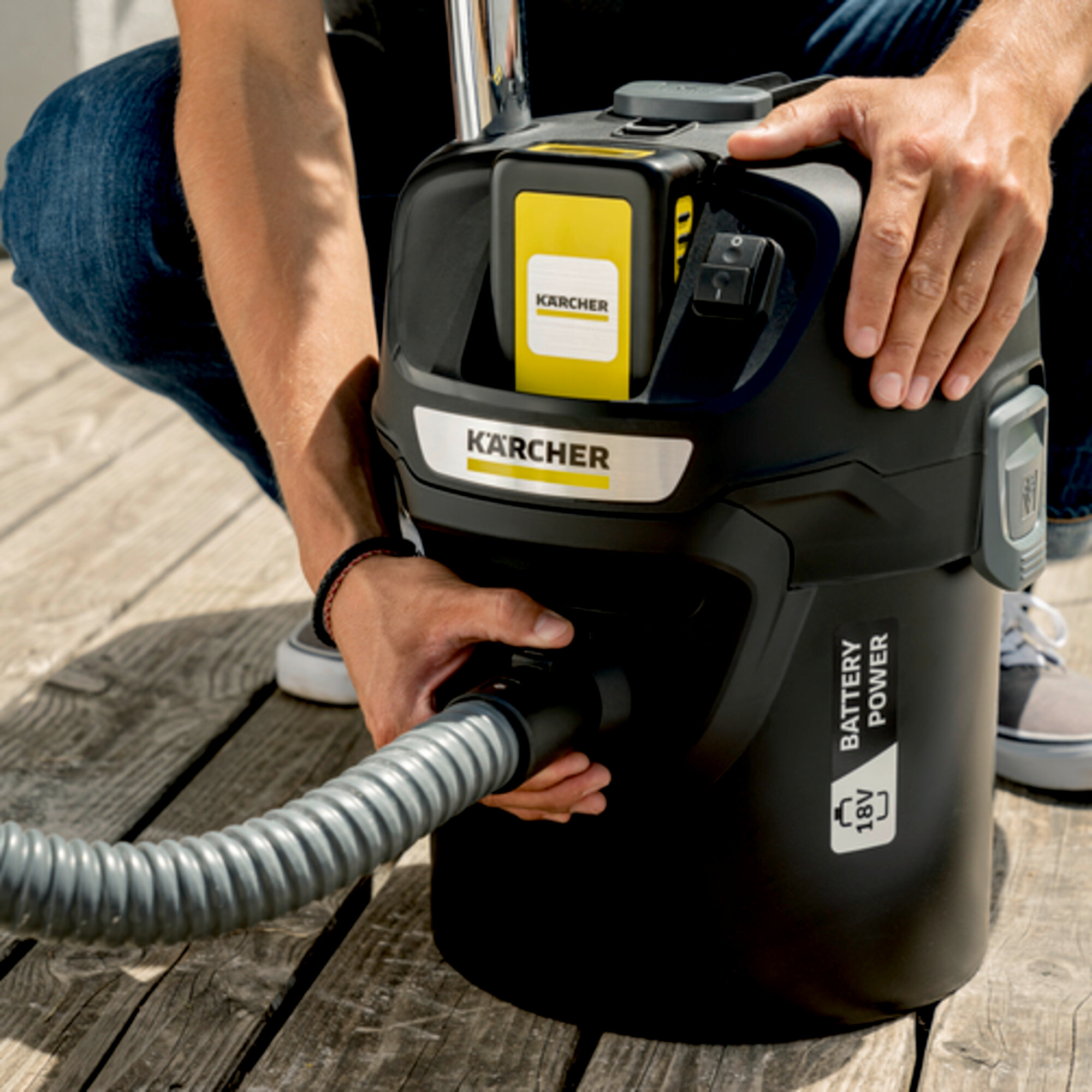 Personne avec aspirateur Kärcher, batterie insérée, tuyau attaché.