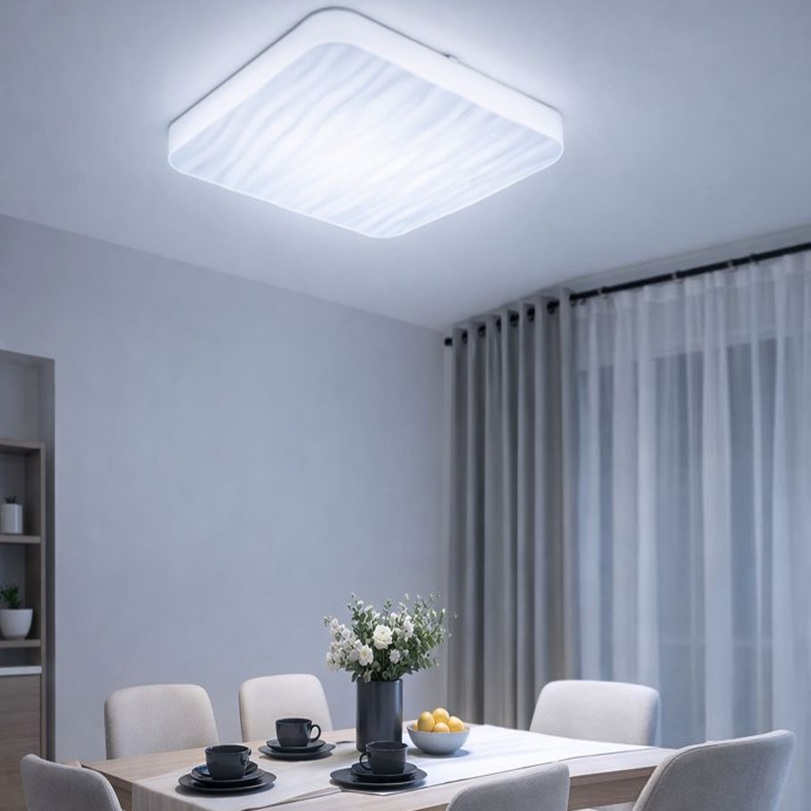 Una lámpara de techo moderna ilumina una mesa de comedor con flores y platos.