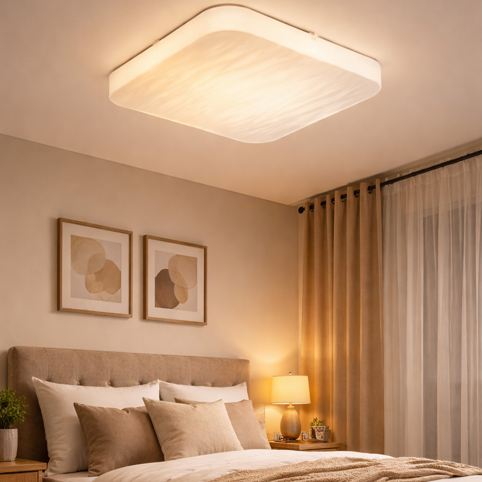 Una escena de dormitorio con cama, mesitas de noche, obras de arte y cortinas bajo una lámpara de techo.