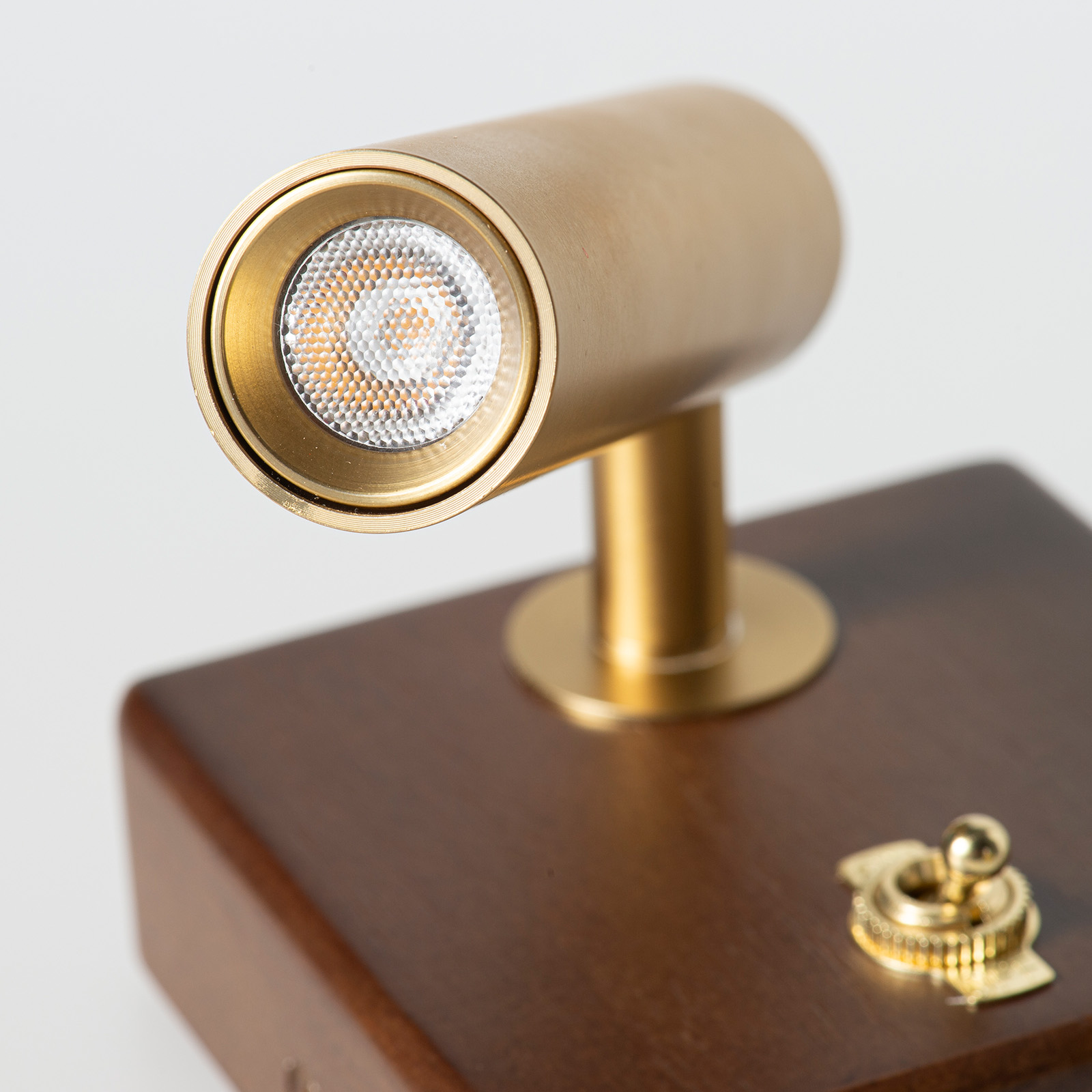 Una lámpara de latón con luz LED sobre base de madera con interruptor.