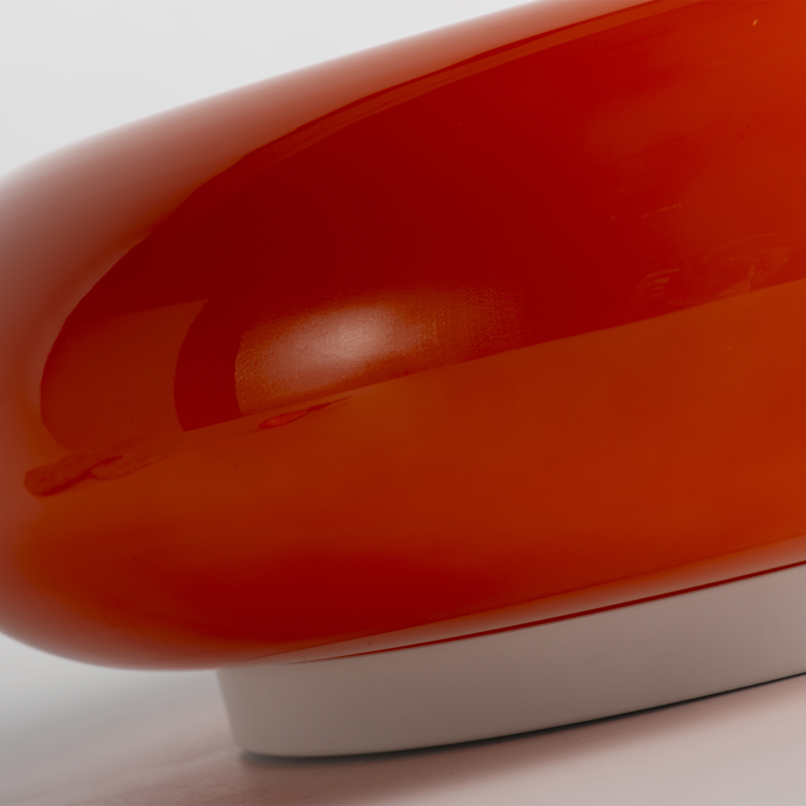 Primer plano de un objeto rojo anaranjado brillante con base blanca.
