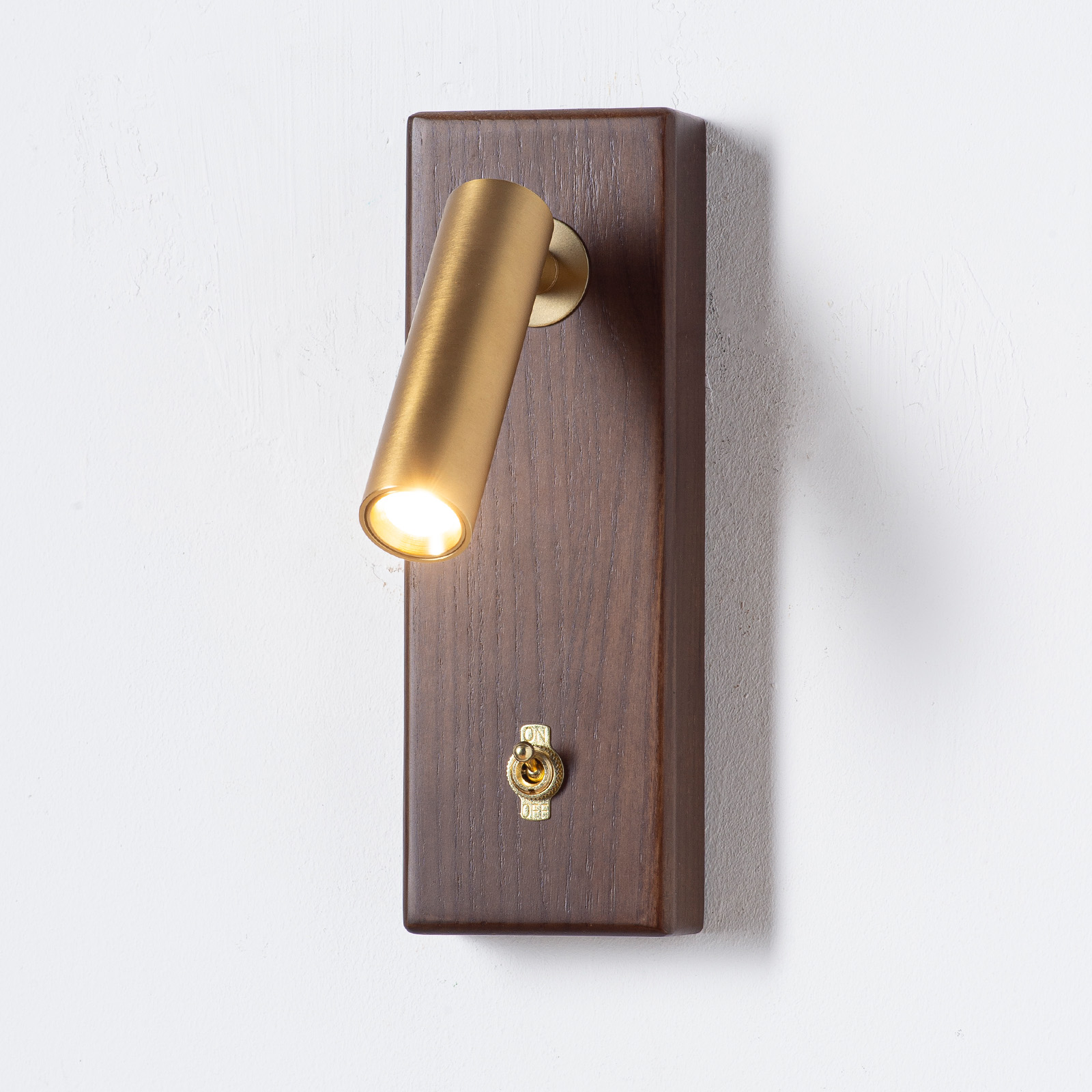 Una lámpara de pared dorada con base de madera y interruptor.