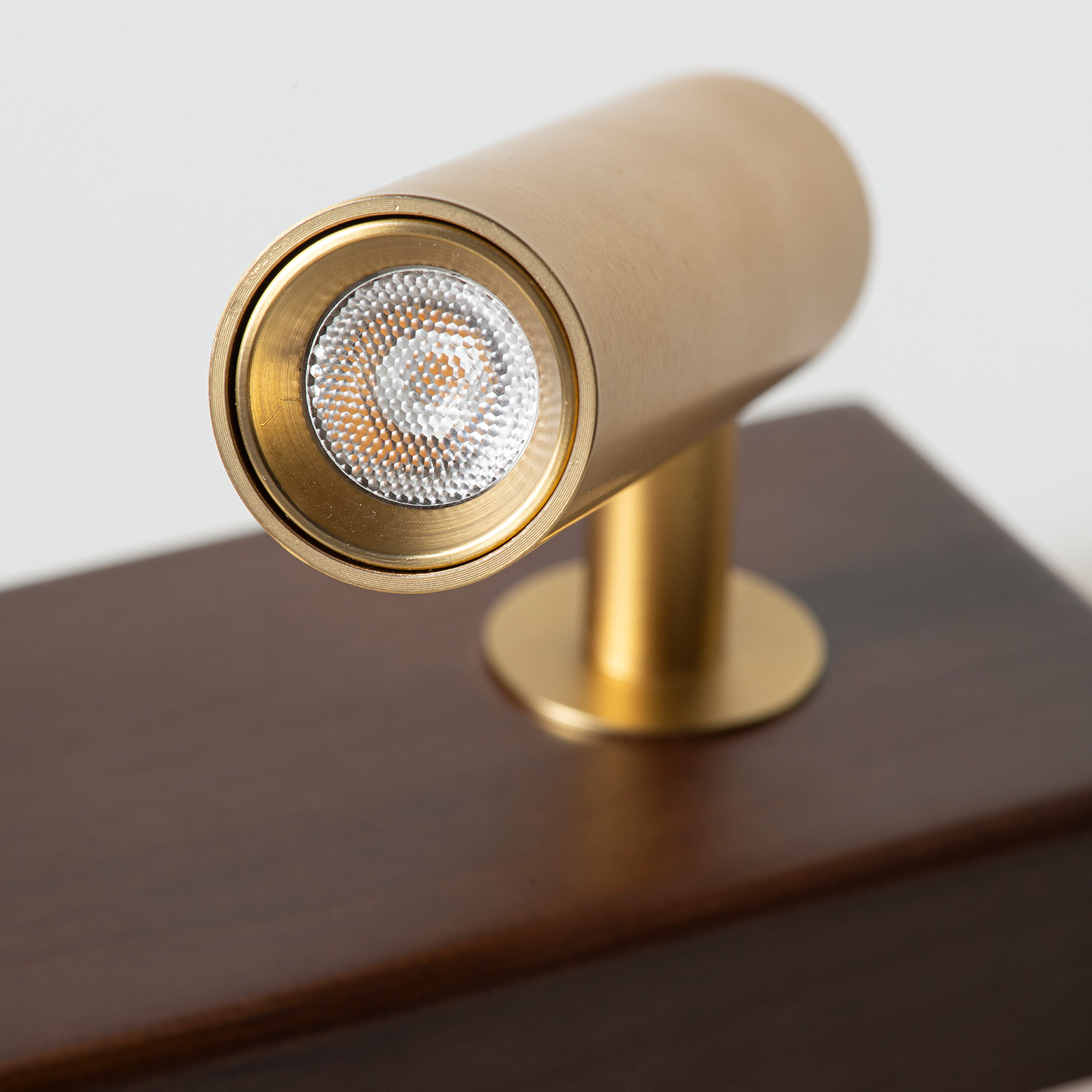 Un foco de latón con luz LED sobre una base de madera oscura.