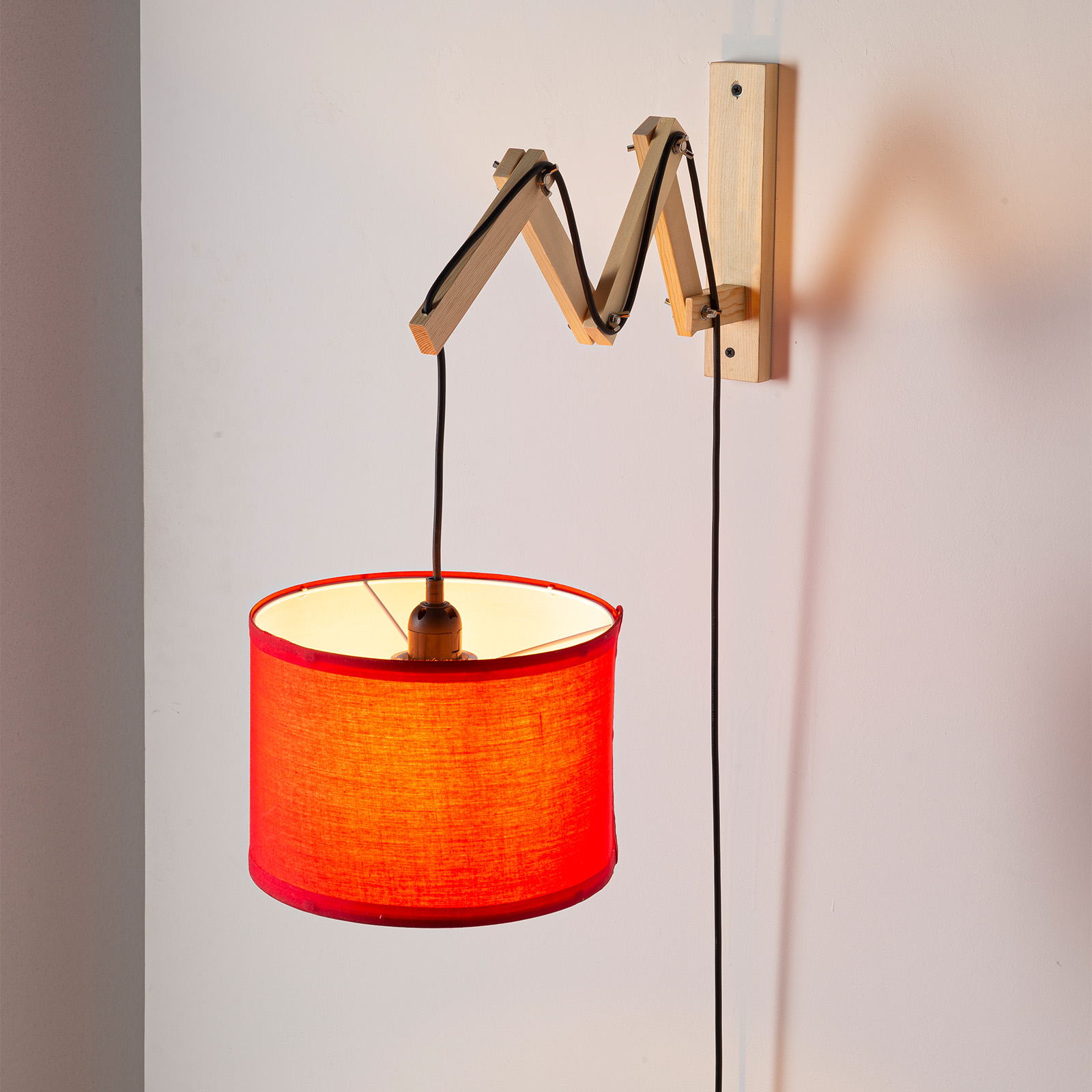 Una lámpara colgante roja con brazo de madera ajustable en una pared.
