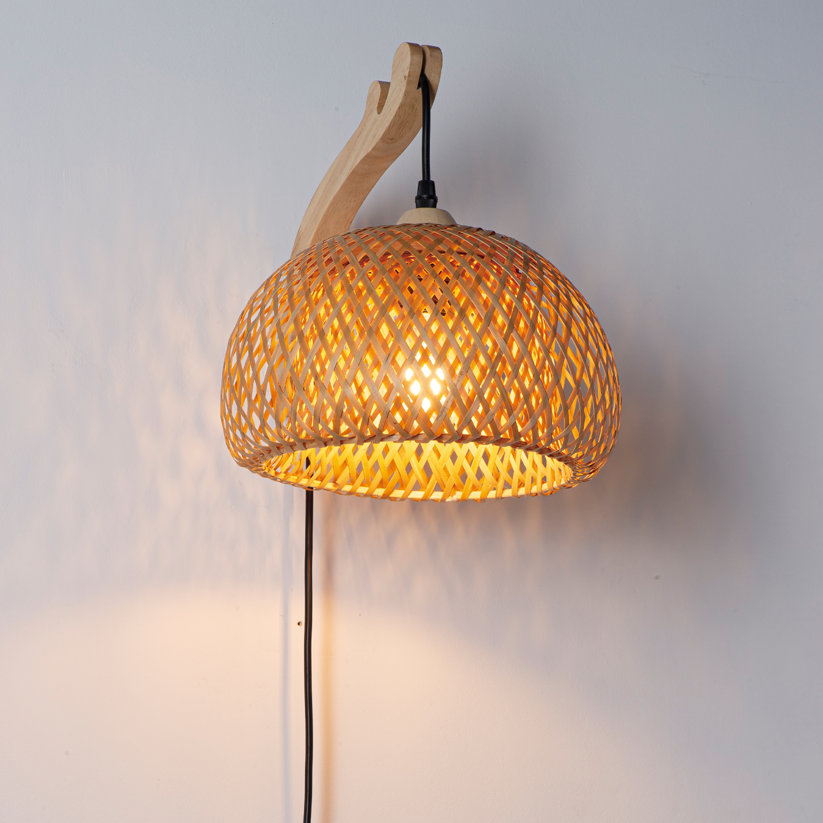 Lámpara de pared de madera con pantalla tejida de bambú, emitiendo luz cálida.