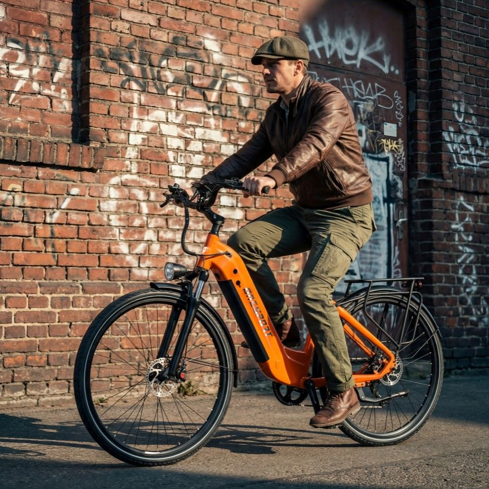 Un uomo guida una bici elettrica arancione davanti a un muro di mattoni con graffiti.