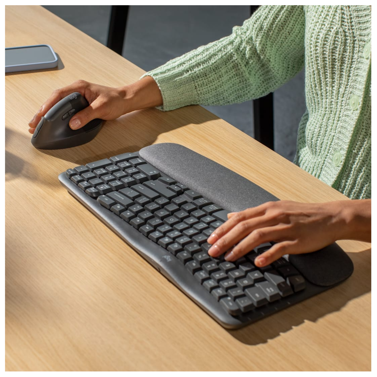 Persona digita su tastiera scura con mouse verticale accanto su scrivania in legno.
