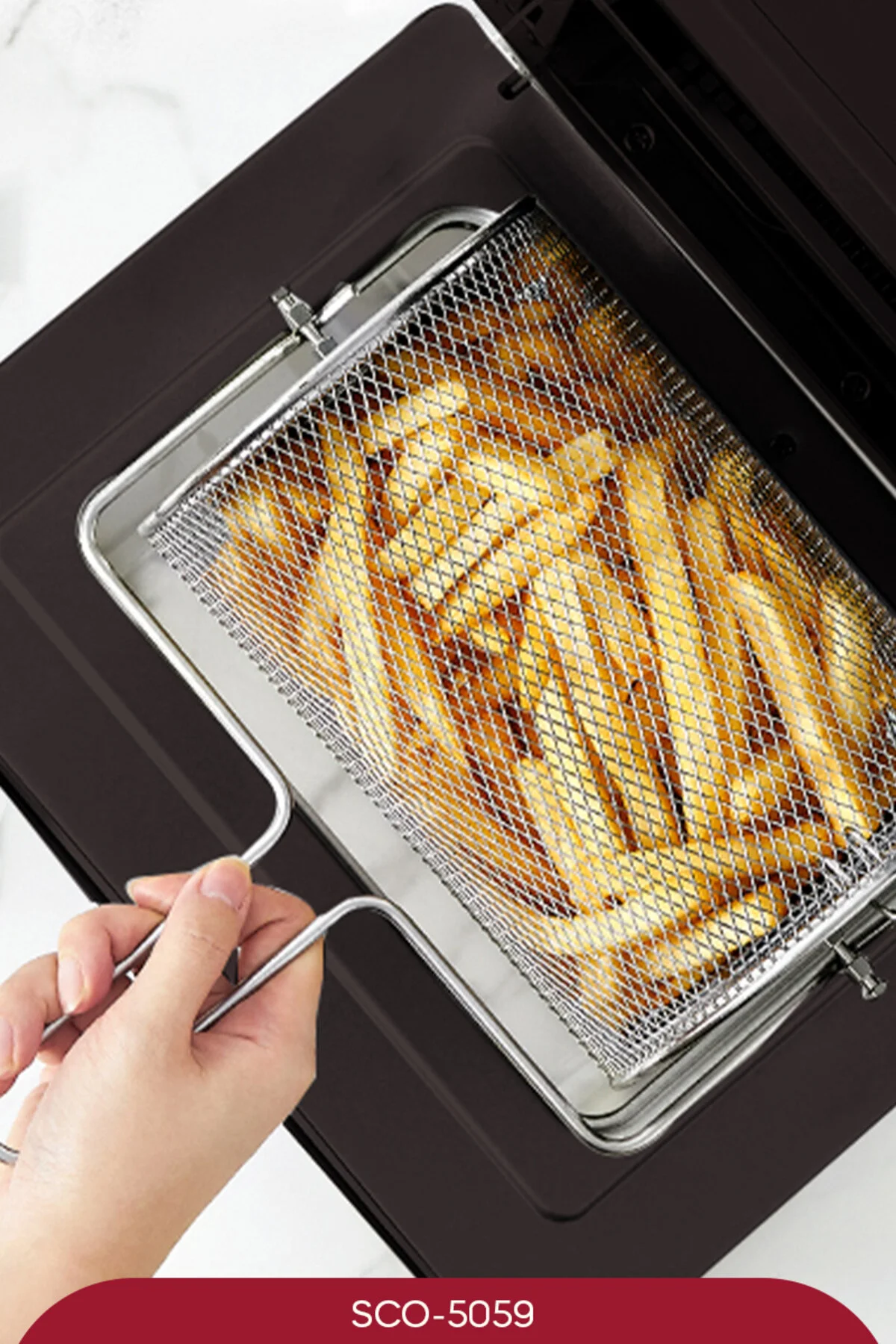 Bir el, airfryer içinde gümüş bir sepette patates kızartması tutuyor.