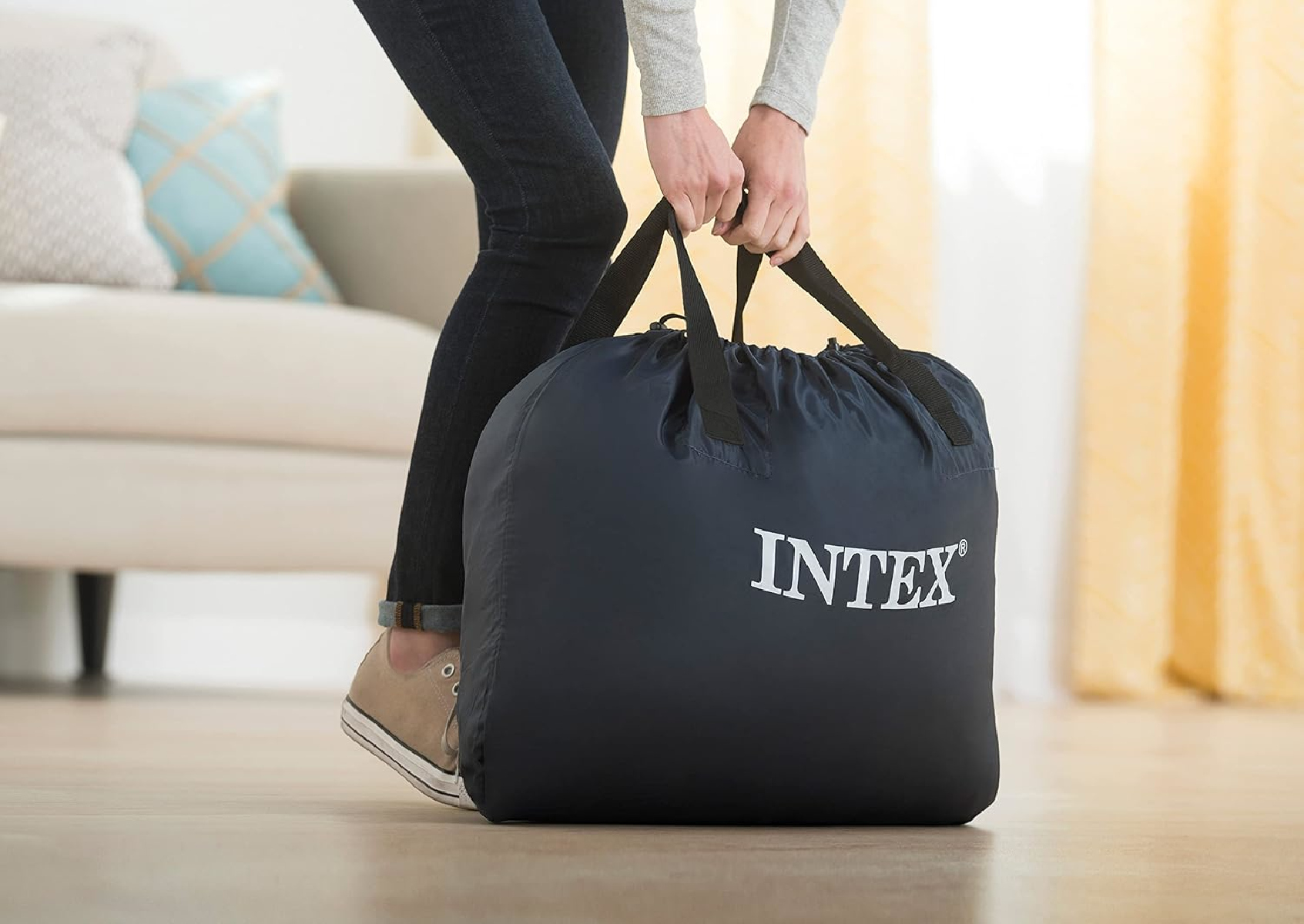 Eine Person trägt eine dunkelblaue Intex-Tasche in einem Wohnzimmer.