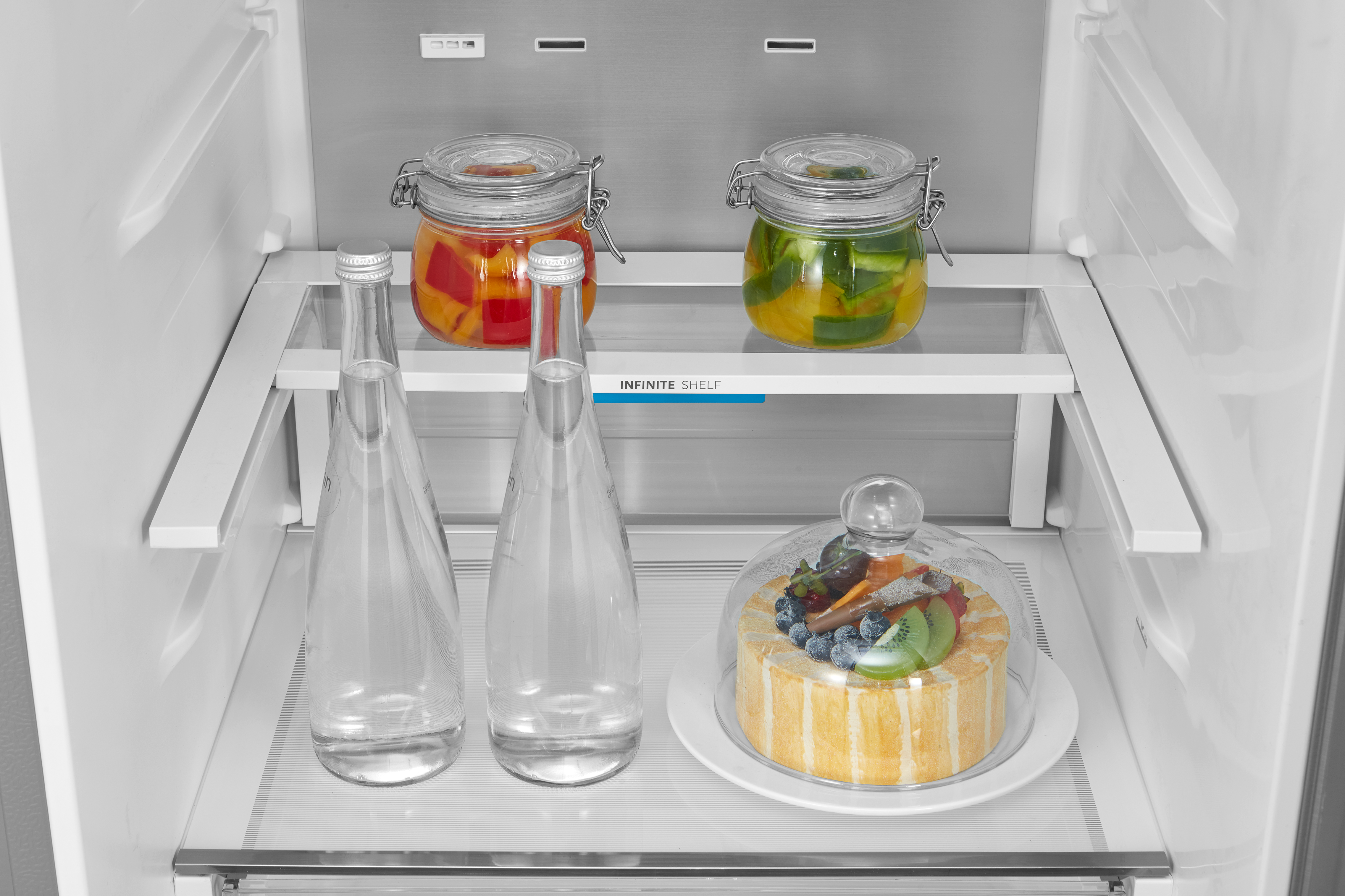 Im Kühlschrank: Glasbehälter mit eingelegtem Gemüse, Wasserflaschen und eine Kuchentorte.