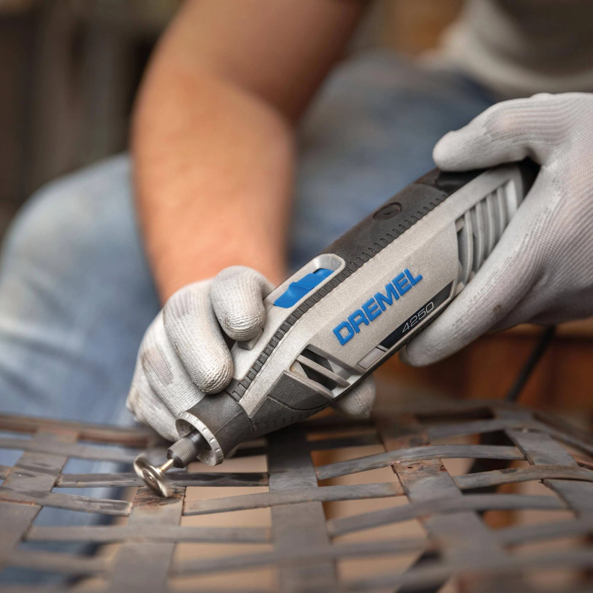 Eine Hand mit Handschuh hält einen Dremel-Schleifer, der auf Metall arbeitet.