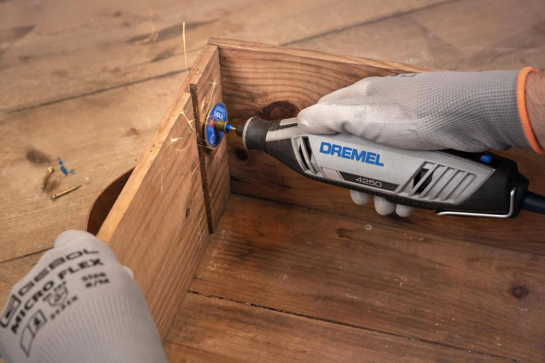 Eine Hand mit Handschuh benutzt einen Dremel-Schleifer an einer Holzkiste.