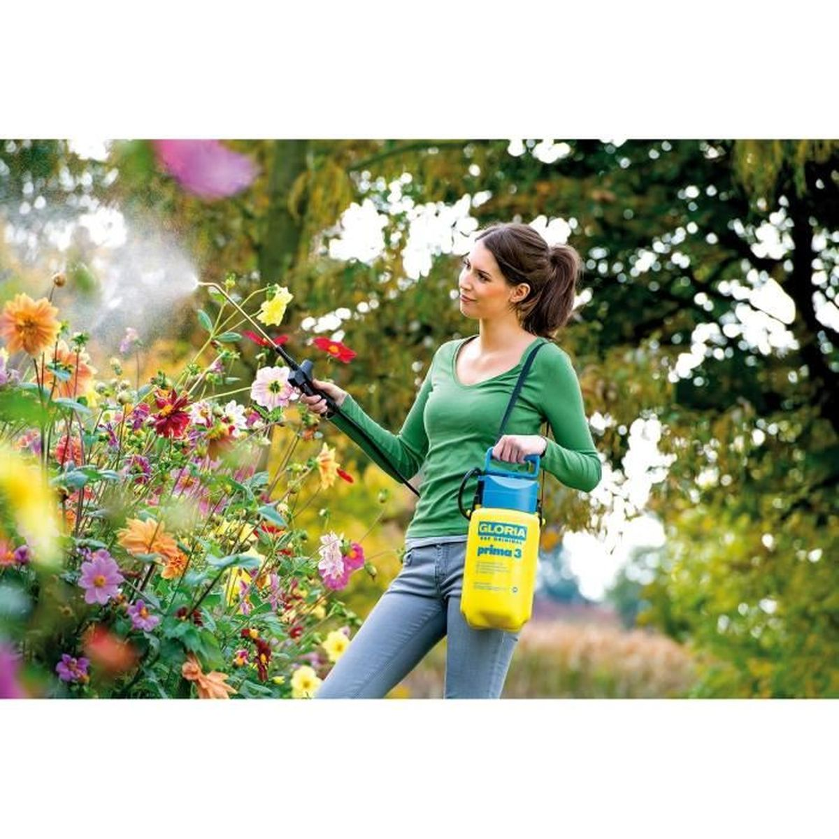 Frau in grünem Hemd sprüht bunte Blumen mit gelbem Sprüher im Garten.