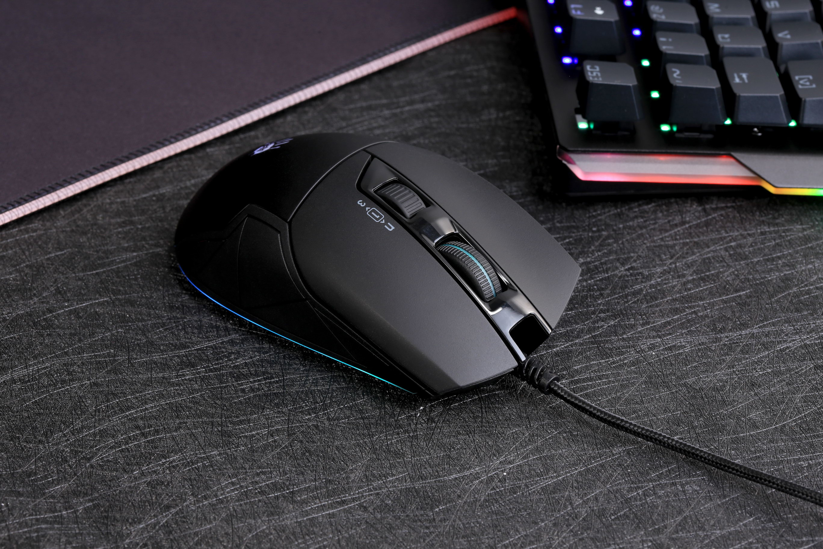 Mouse gaming nero con rotellina, illuminato, accanto a una tastiera.