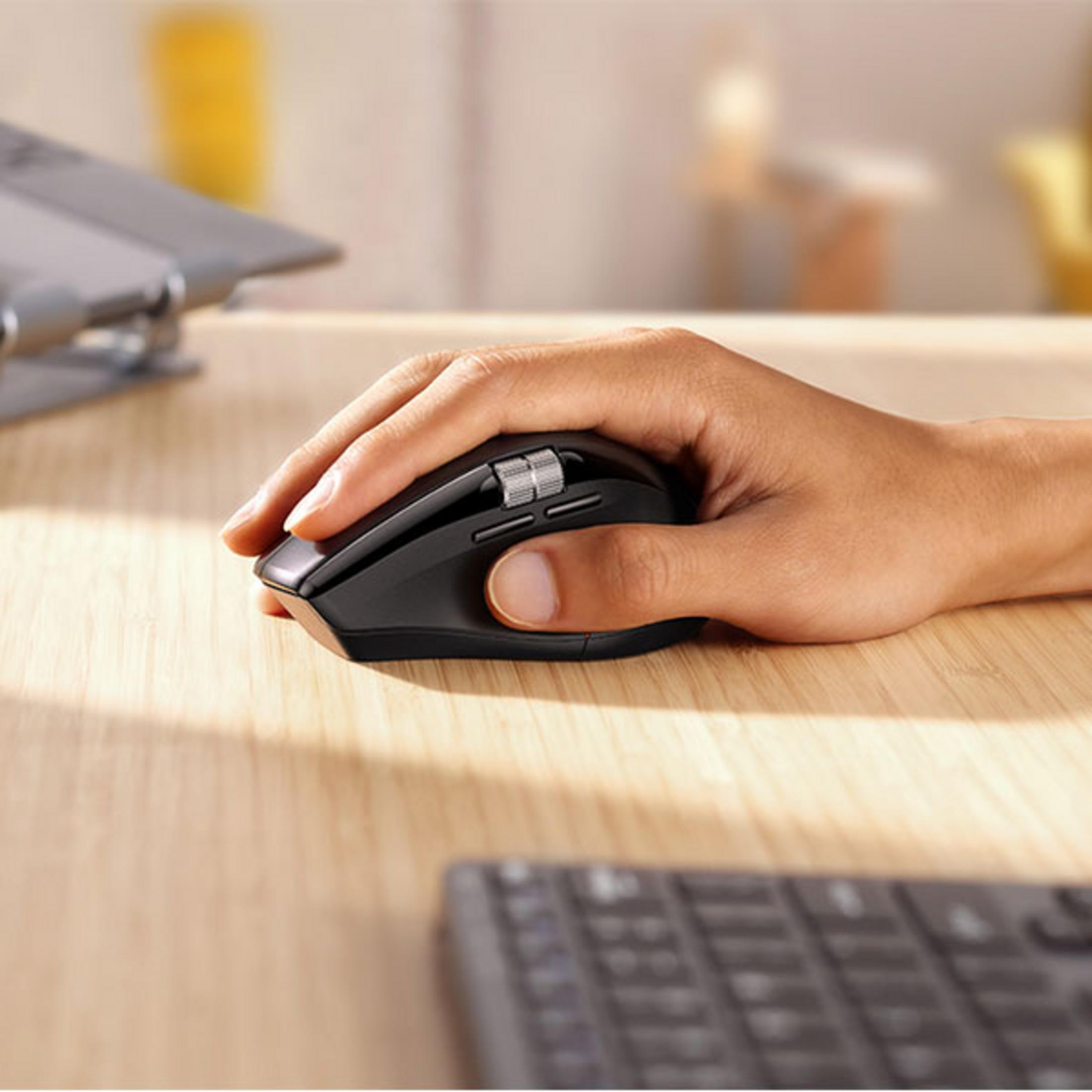 Una mano usa un mouse nero su una scrivania di legno. Tastiera in primo piano.