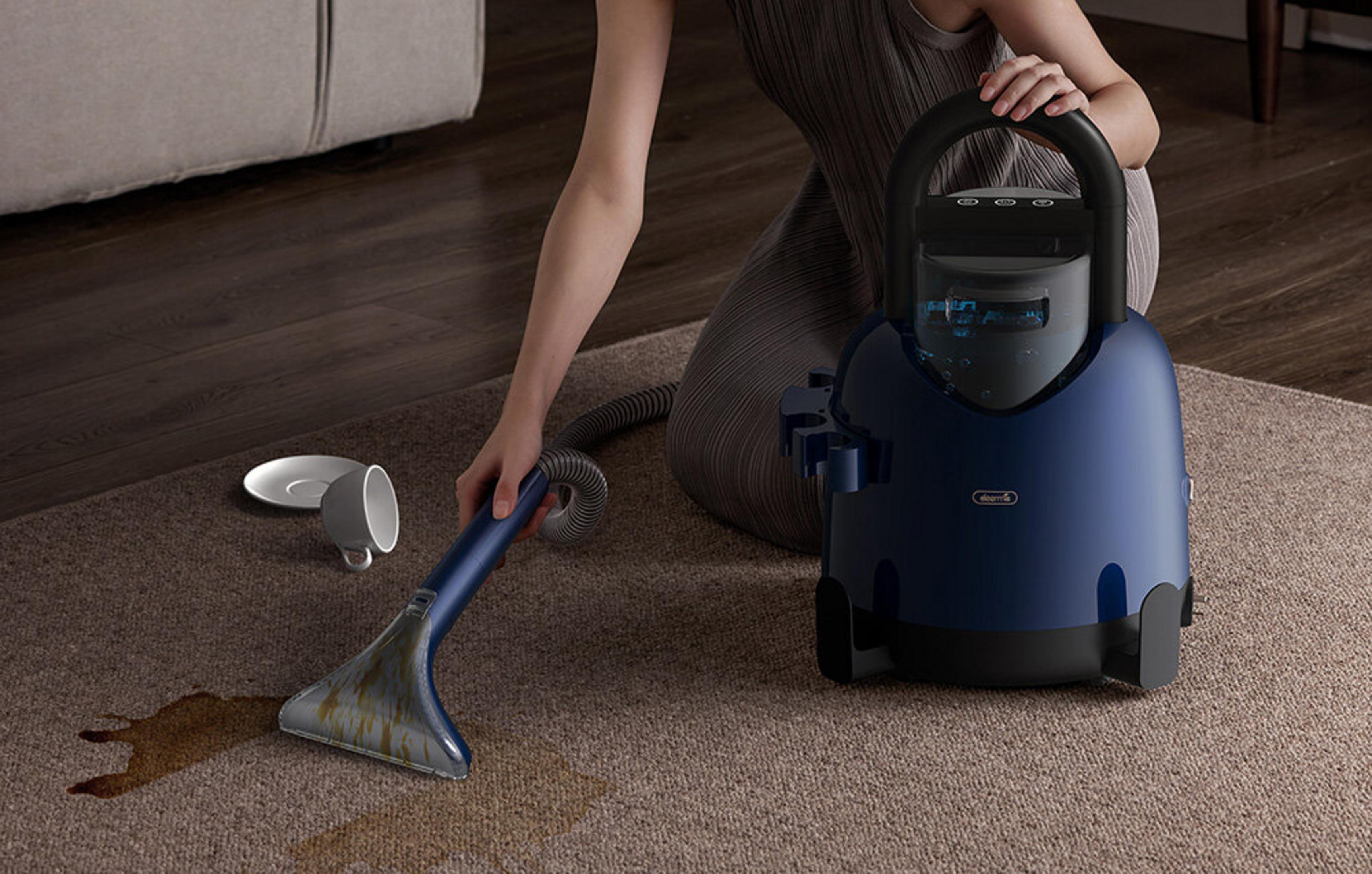 Una donna pulisce una macchia sul tappeto con un aspirapolvere spray blu.
