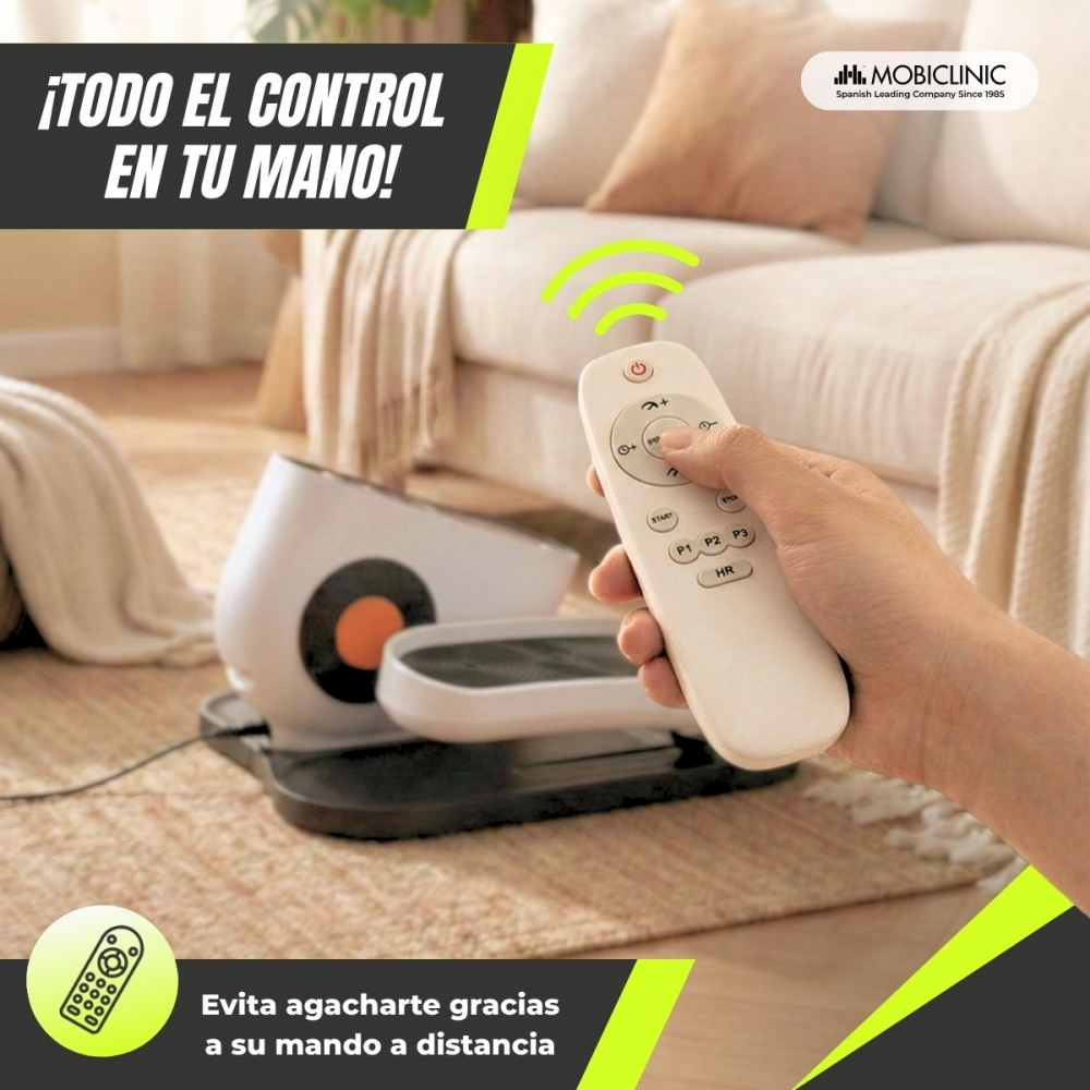 Una mano sostiene un mando a distancia para un aparato de fitness. Un sofá al fondo.