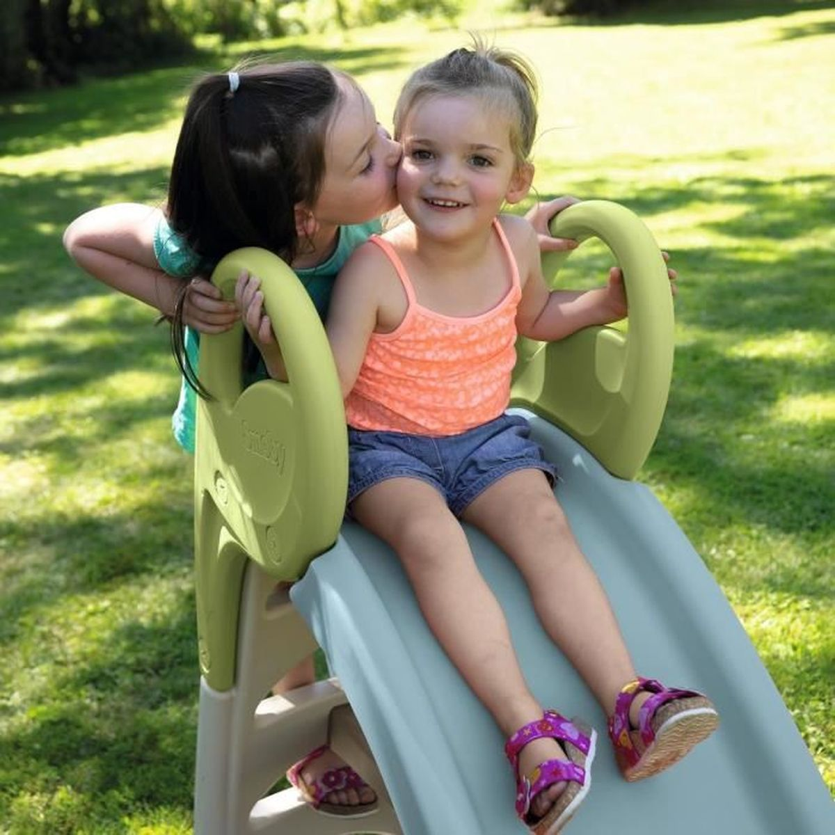 Una bambina ne bacia un'altra su uno scivolo in giardino.