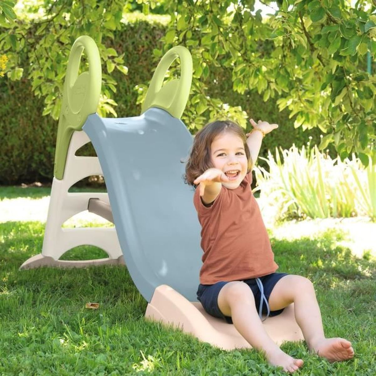Un bambino felice seduto su uno scivolo azzurro in un giardino.
