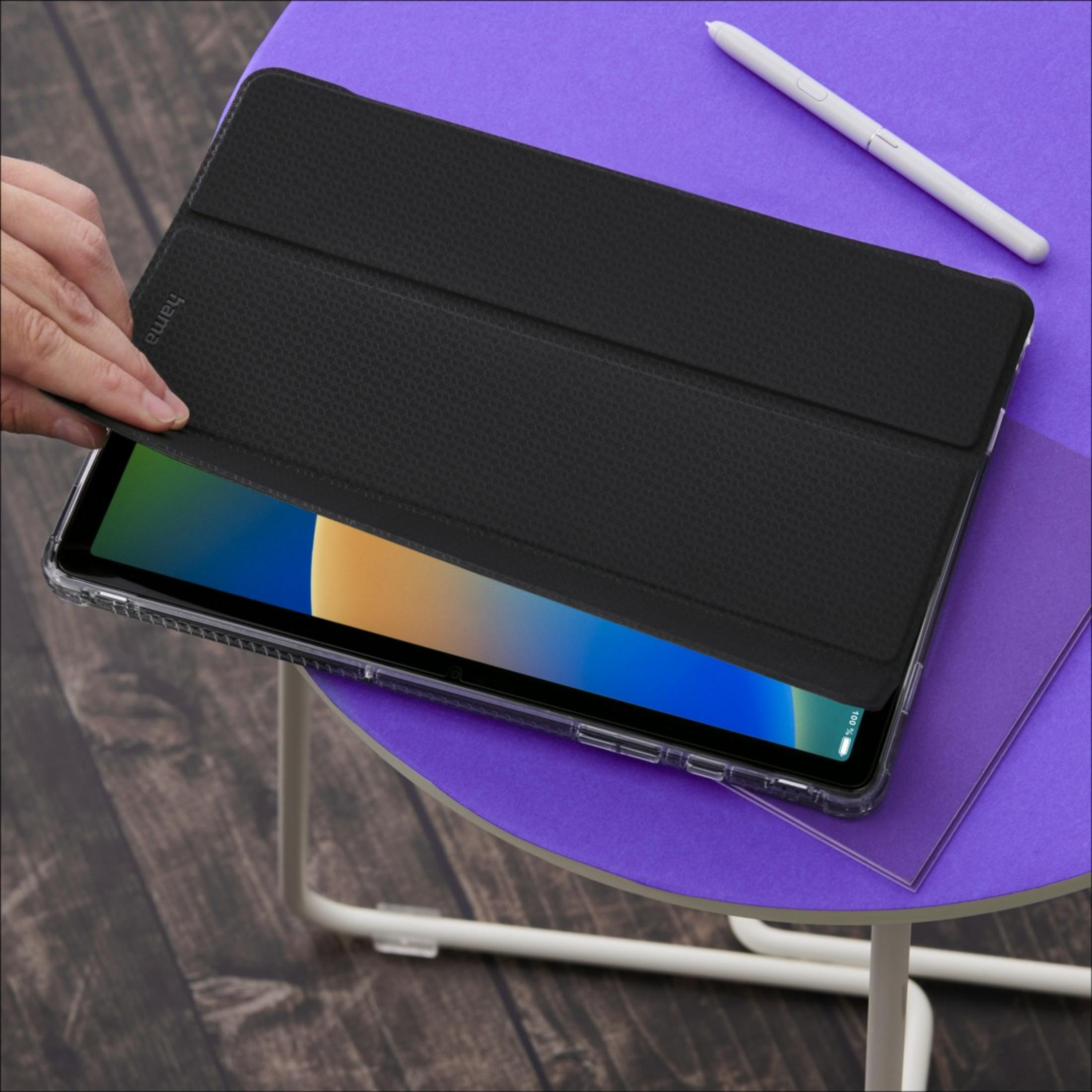 Dłoń otwiera czarne etui na tablet na fioletowym stole obok rysika.