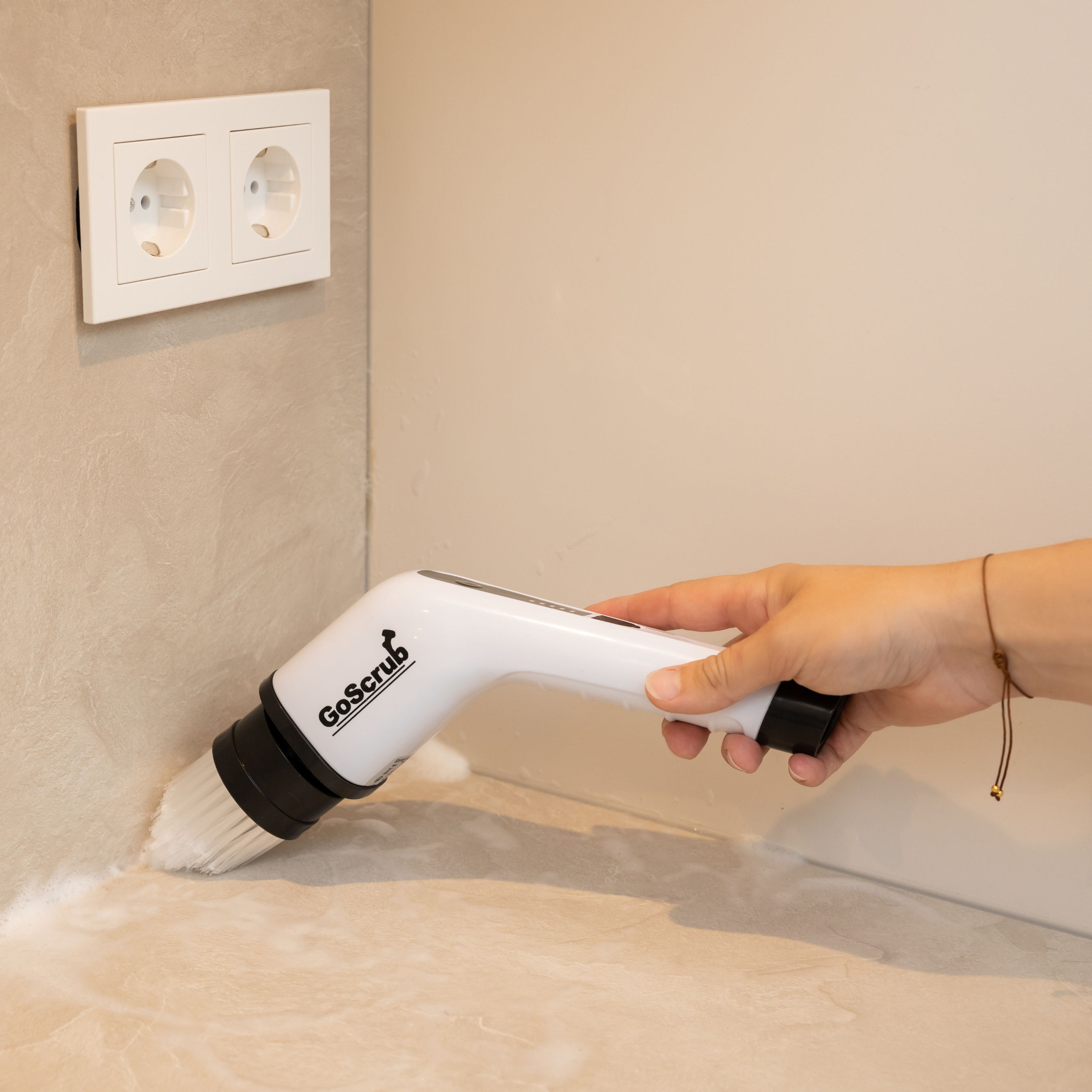 Een hand houdt een witte elektrische borstel vast die een aanrecht schoonmaakt met sop.