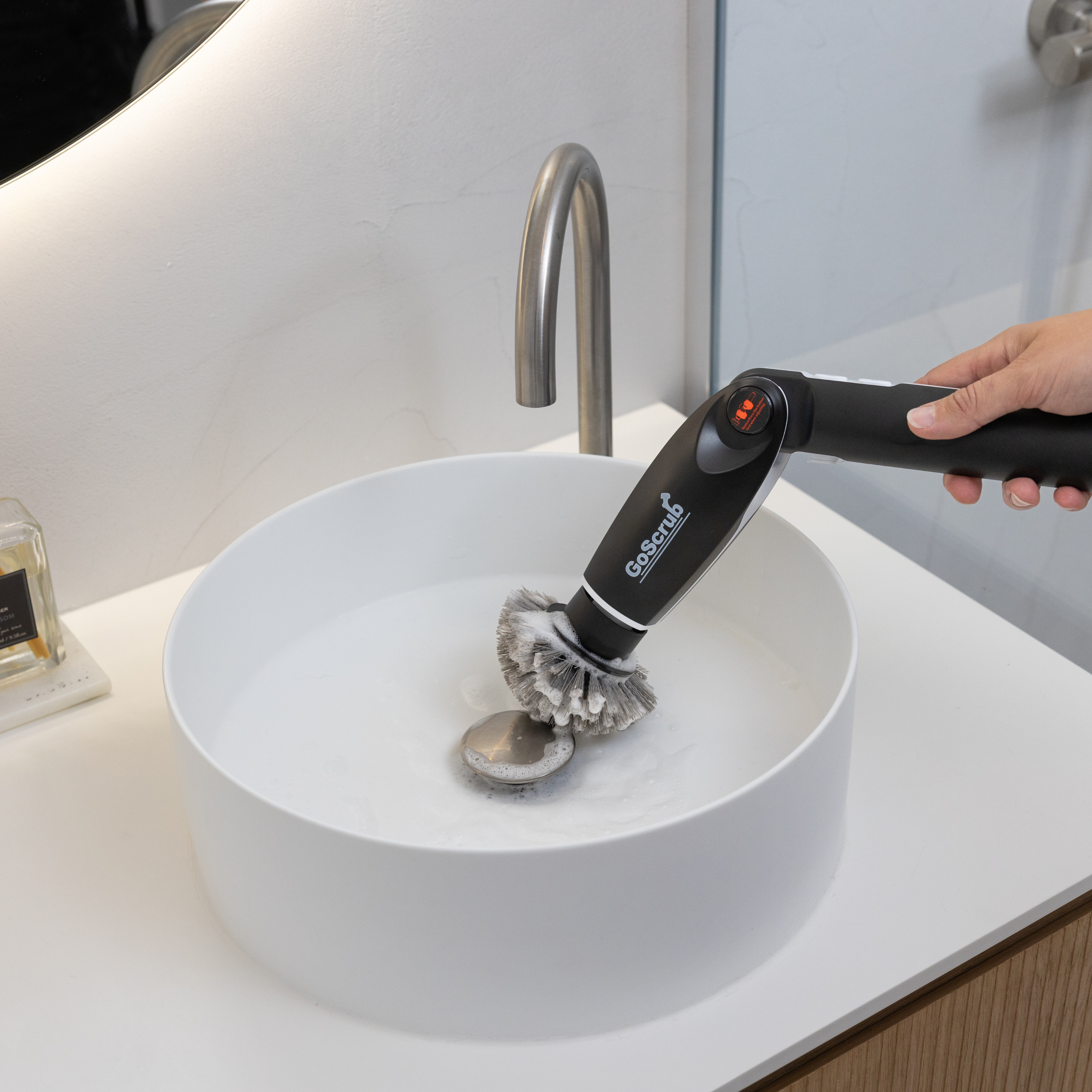 Een hand houdt een elektrische borstel boven een witte wastafel met water.