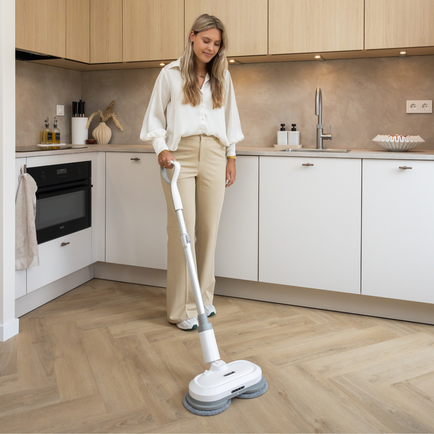 A woman mops the floor with a mop in a modern kitchen.