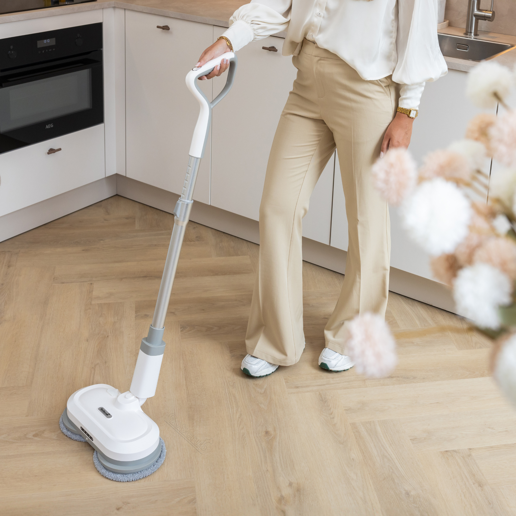 A woman cleans a wood floor in a kitchen with a spinning mop.
