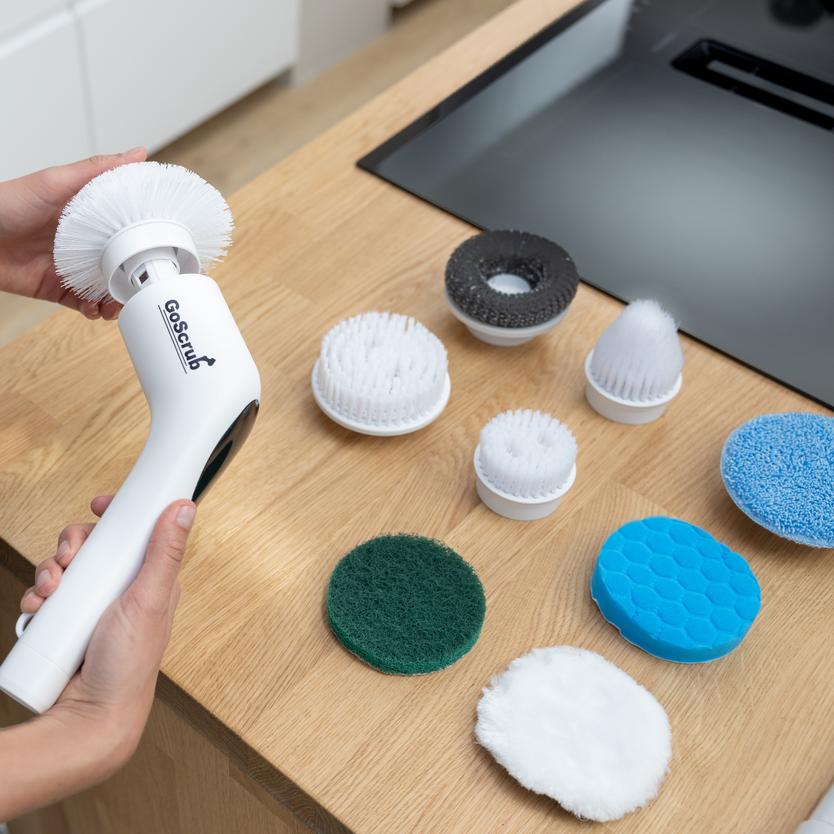 Een witte elektrische schrobber met diverse opzetstukken op een houten aanrecht.