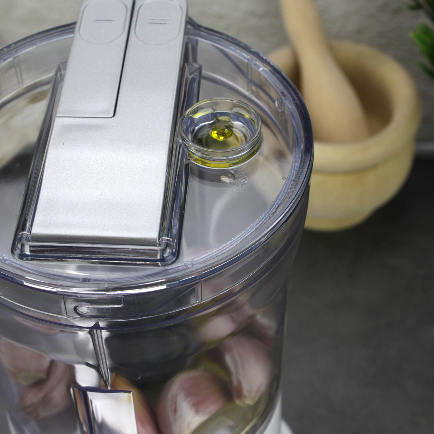 Un procesador de alimentos con ajo y aceite, un mortero al fondo.