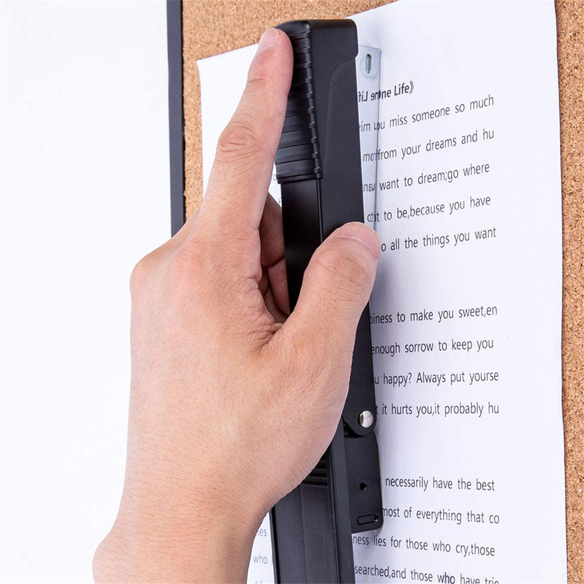 Eine Hand benutzt einen schwarzen Locher auf einem Blatt Papier, das an einer Pinnwand hängt.