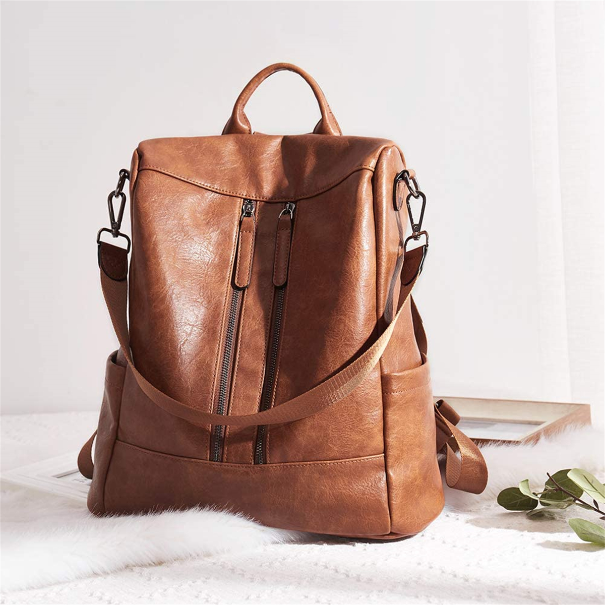 Brauner Rucksack mit Reißverschlüssen und Seitentaschen, auf weißem Fell.