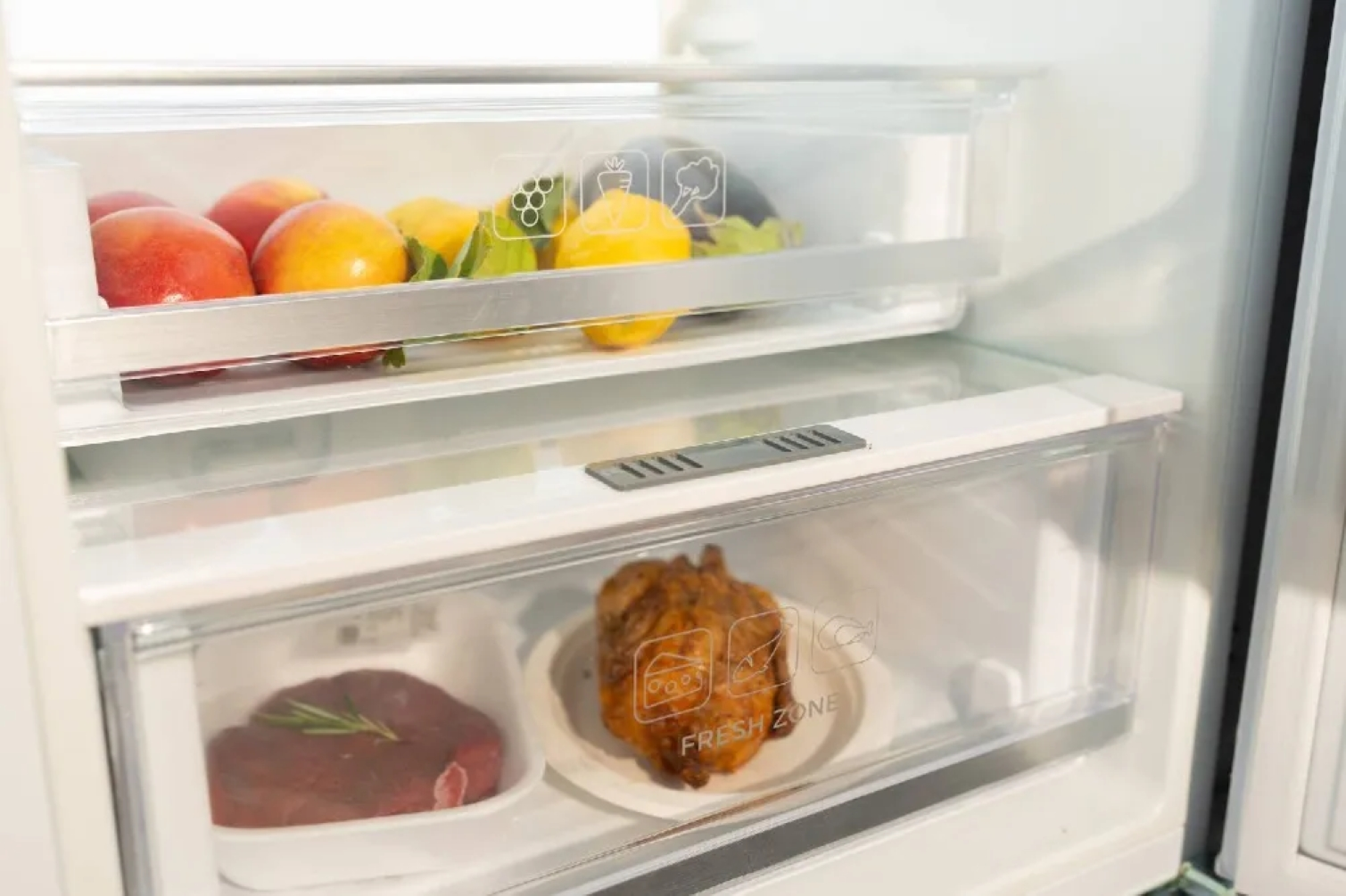 Interno di un frigorifero: frutta fresca nel cassetto superiore, carne cruda e pollo cotto nel cassetto inferiore.