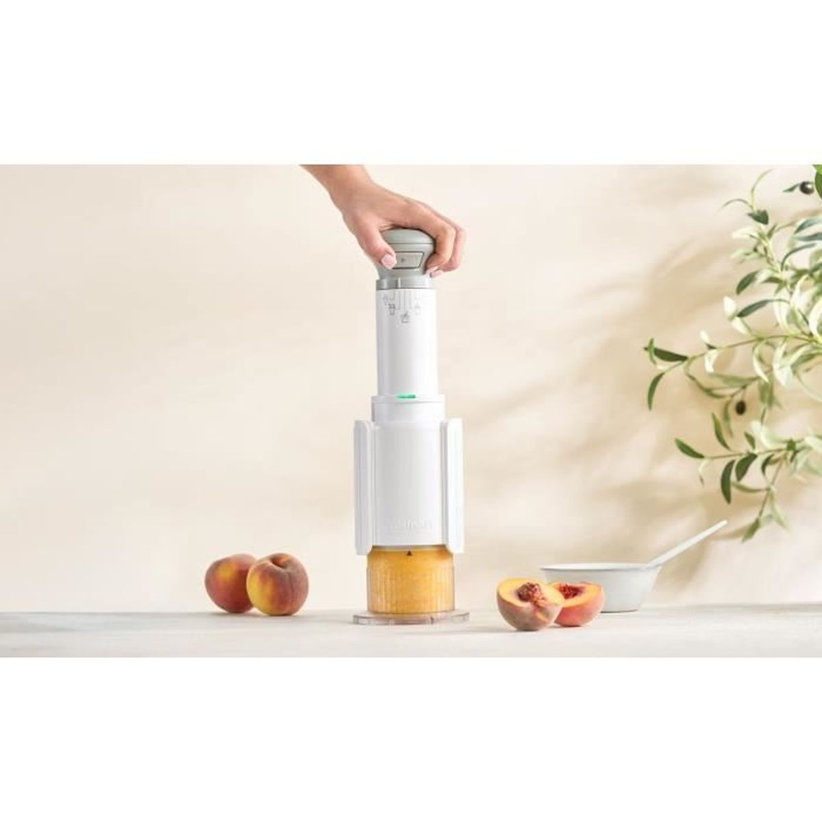 Un passaverdure bianco su un tavolo con pesche intere e dimezzate.