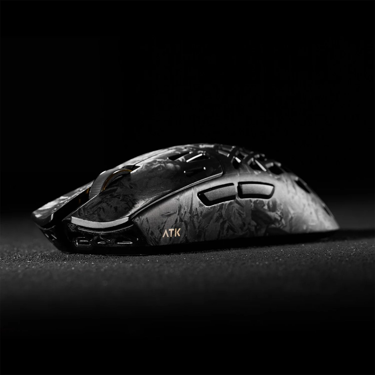 Een zwarte gamingmuis met getextureerde afwerking en gouden ATK-logo op donkere achtergrond.