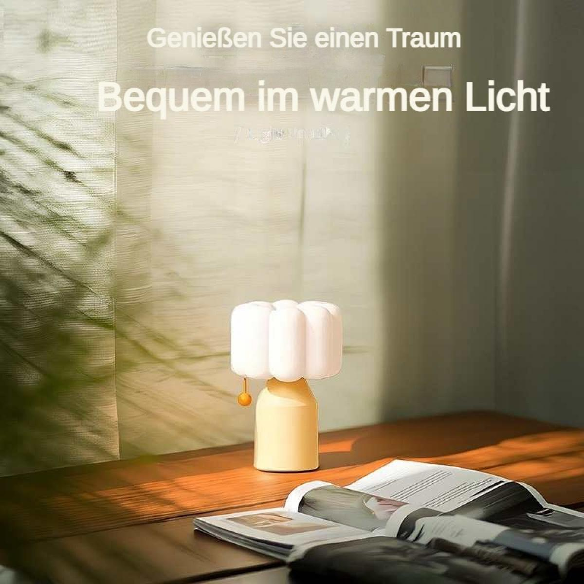 Eine gelbe Lampe mit weißem Lampenschirm steht auf einem Holztisch neben einem Buch.