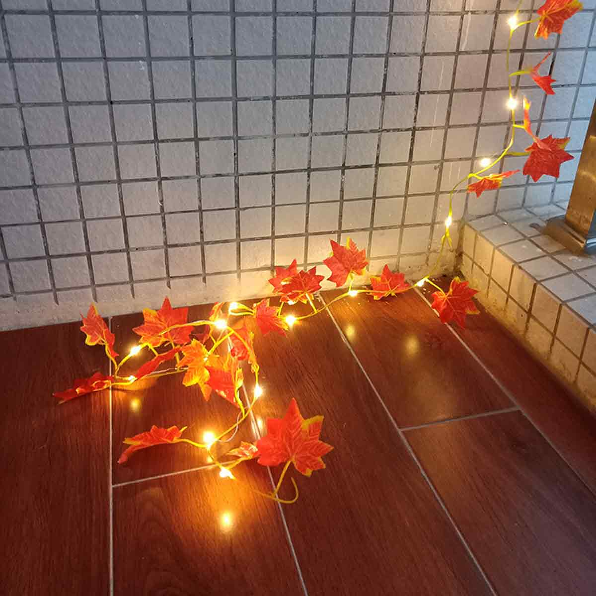 Kette aus roten Ahornblättern mit Lichterkette auf Holzboden und Kachelwand.