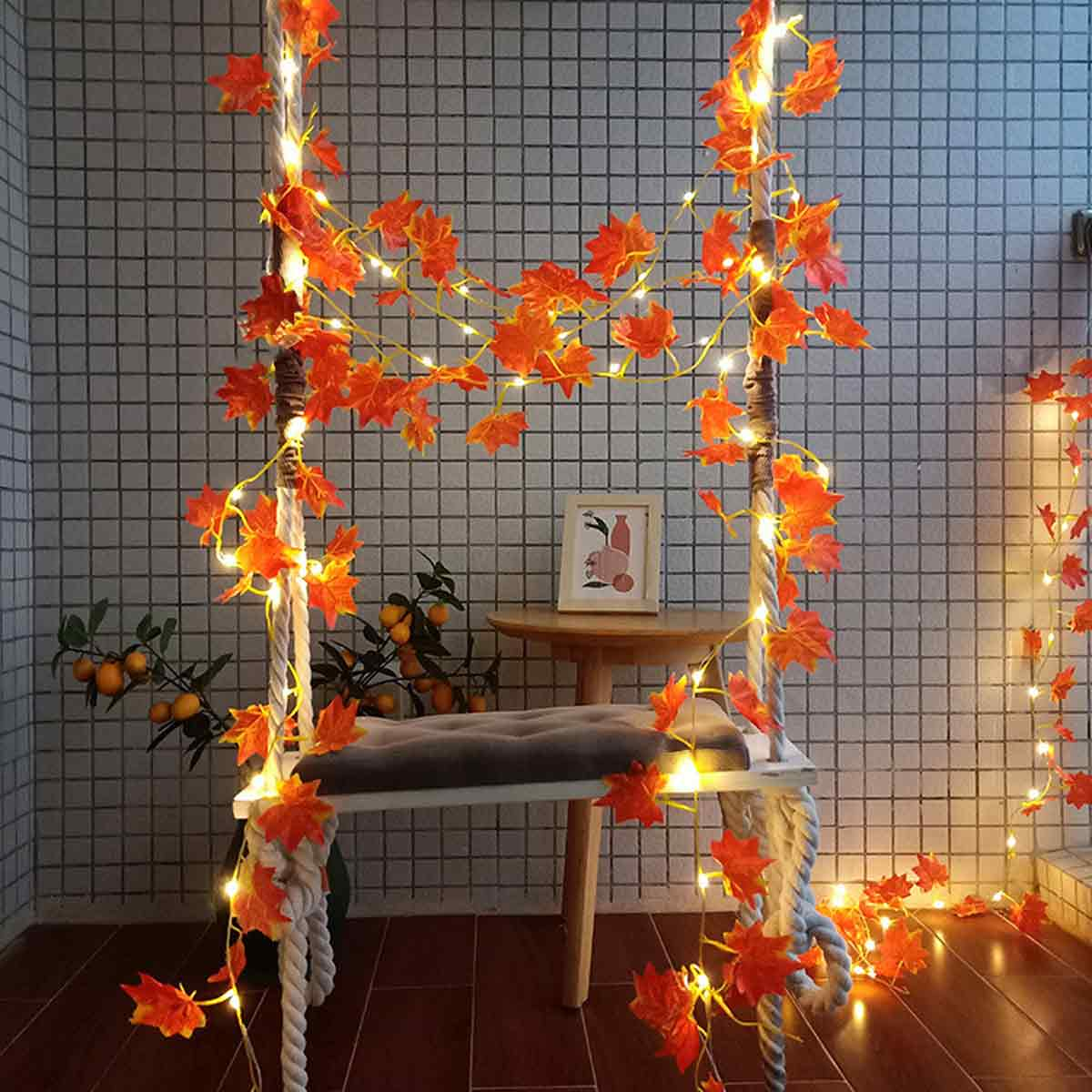 Eine Schaukel mit Lichterkette und Herbstblättern. Ein kleiner Tisch steht daneben.