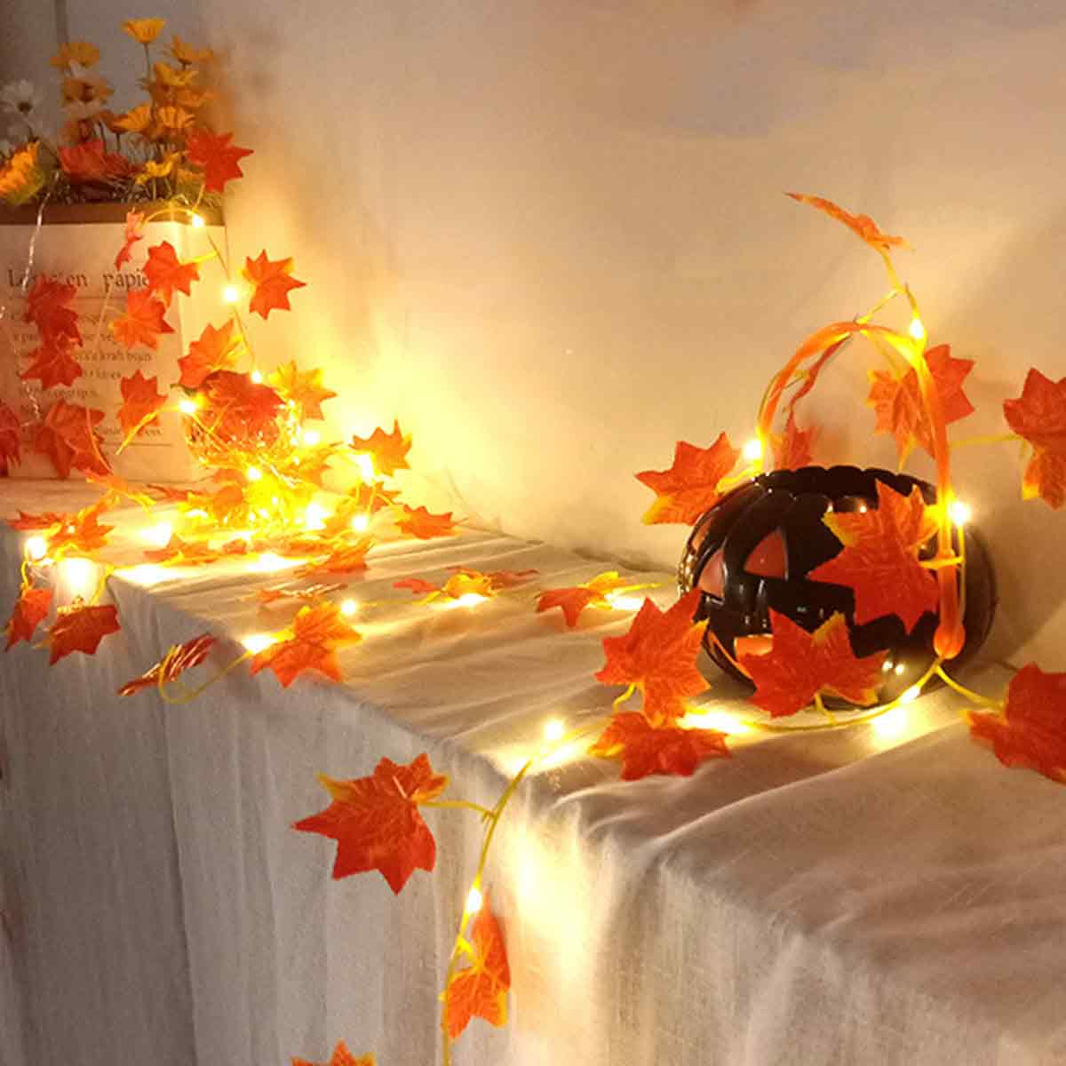 Halloween-Deko mit Kürbis, Blättern und Lichterkette auf Tisch.