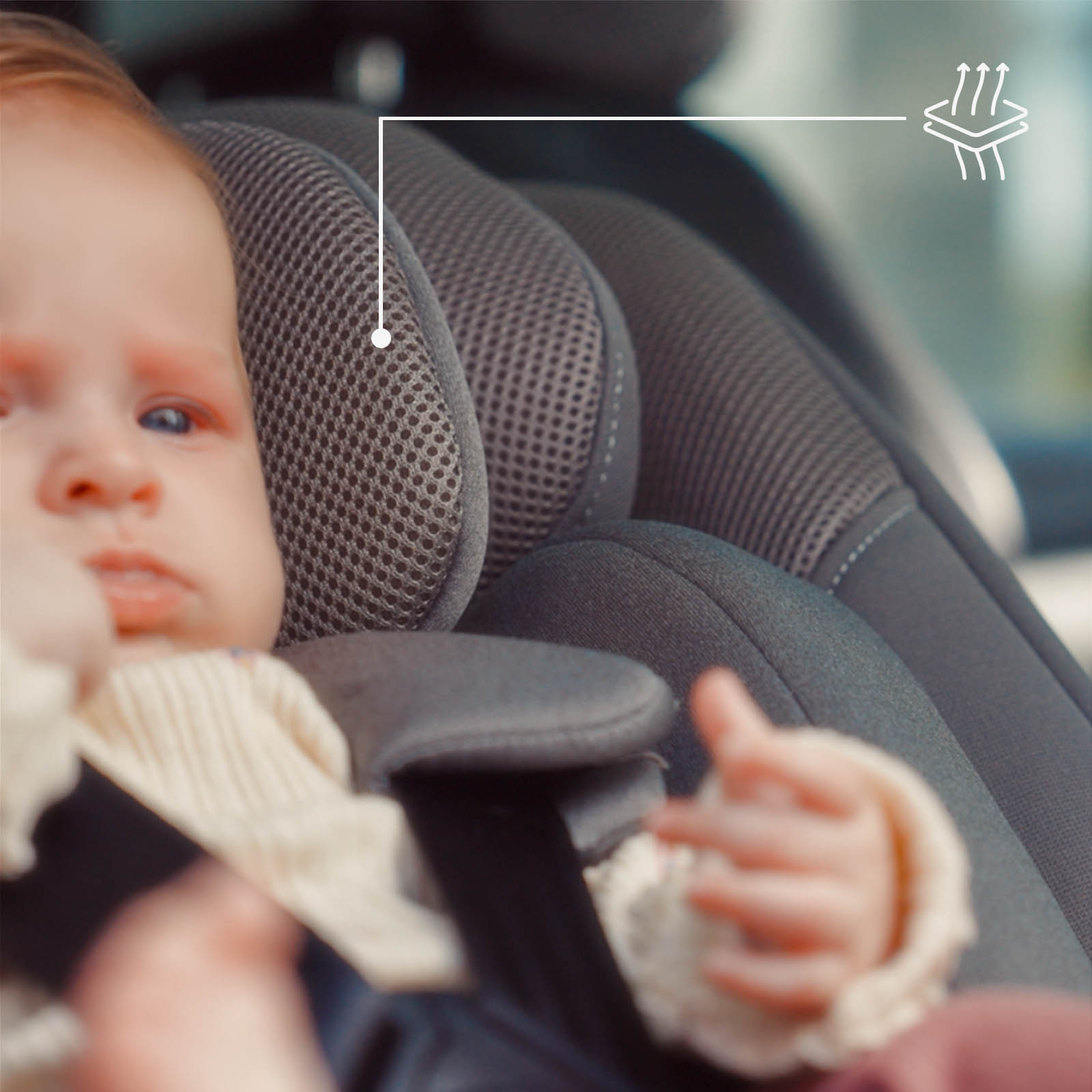 Ein Baby sitzt in einem Autositz mit Netzstoff-Akzenten und einem Belüftungssymbol.