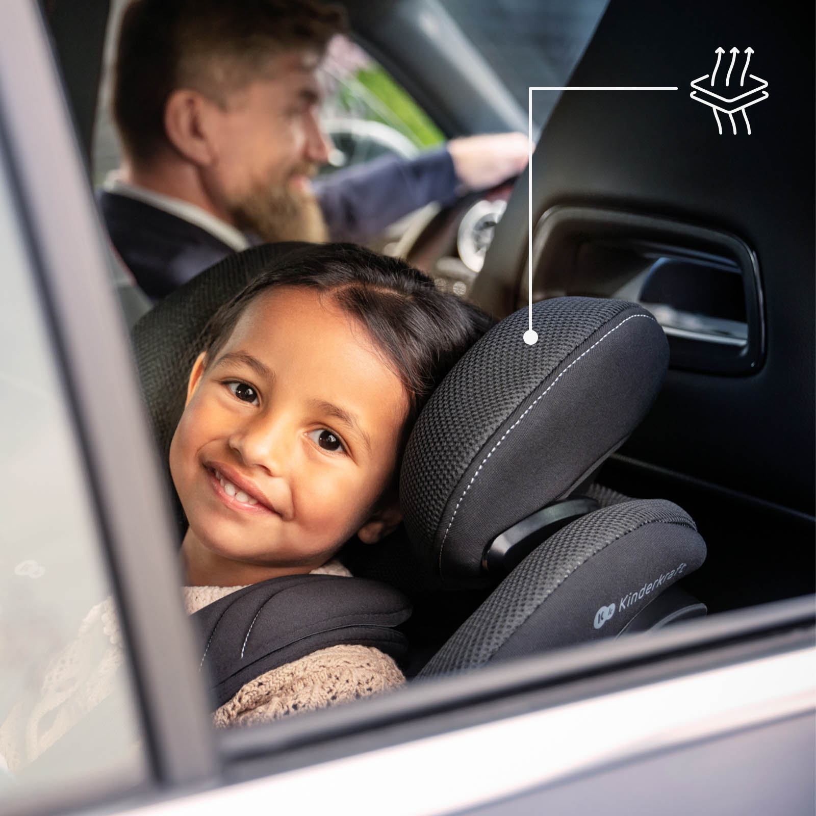 Ein Mädchen sitzt in einem Autositz, ein Mann fährt im Hintergrund.