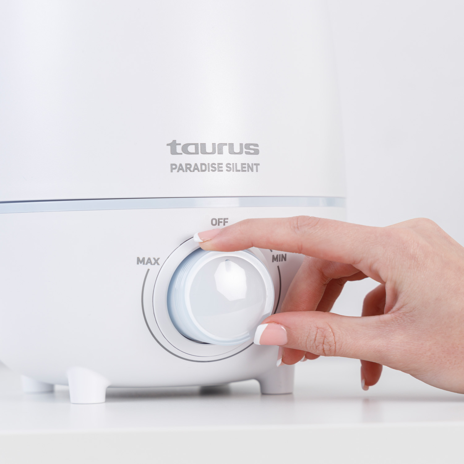 Una mano gira un dial blanco en un aparato blanco con la etiqueta 'TAURUS'.