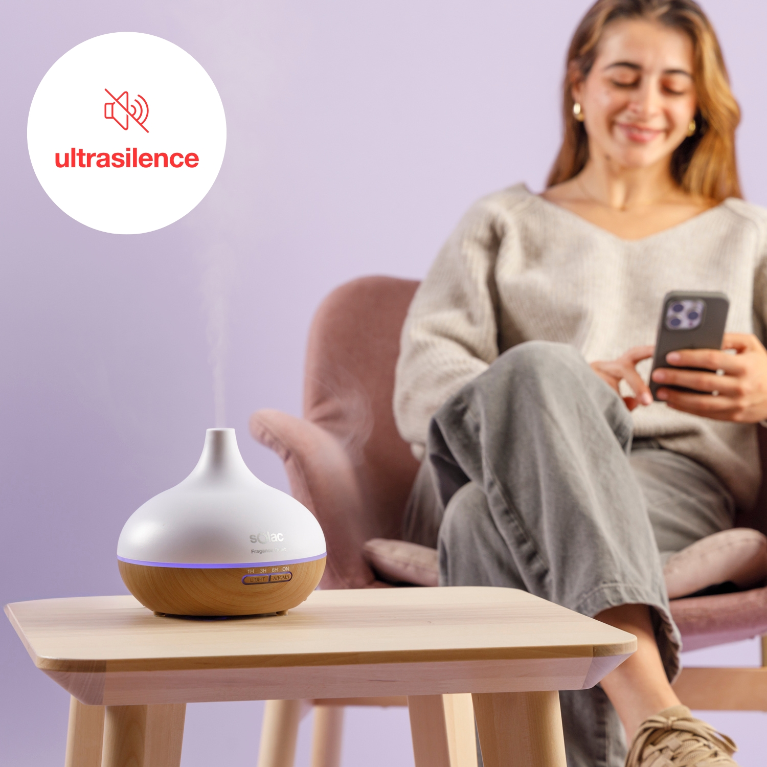 Un difusor emitiendo vapor en una mesa de madera, una mujer mira su teléfono.