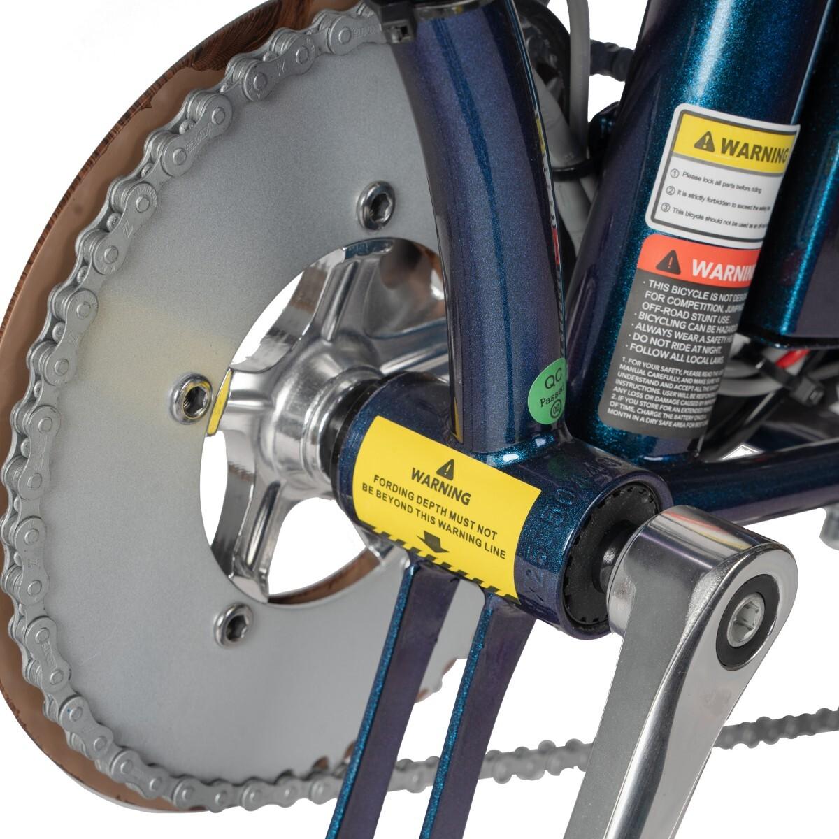 Zbliżenie łańcucha i korby roweru z żółtymi naklejkami ostrzegawczymi.