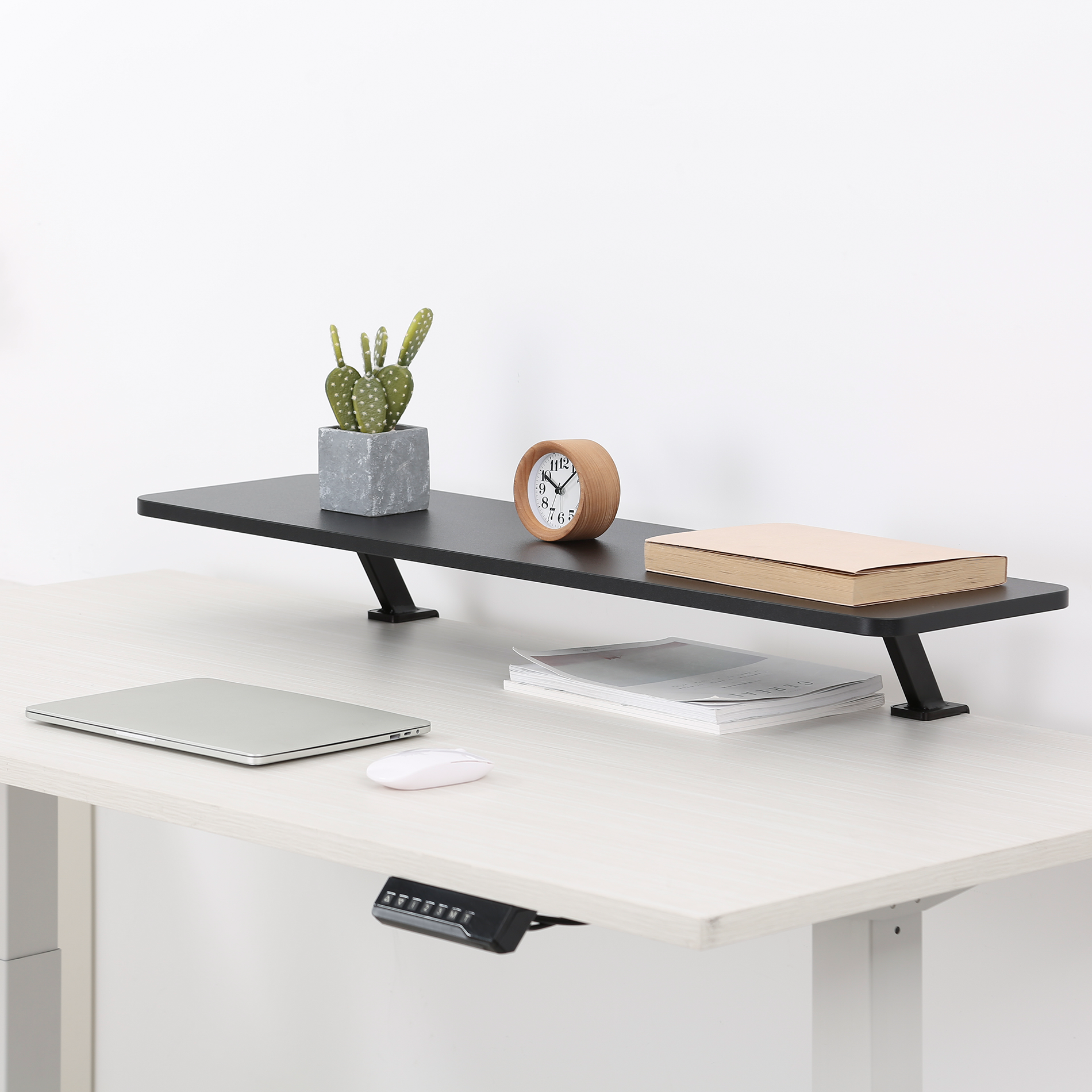 Escritorio con soporte para monitor que tiene una planta, reloj y libro. Portátil y ratón.