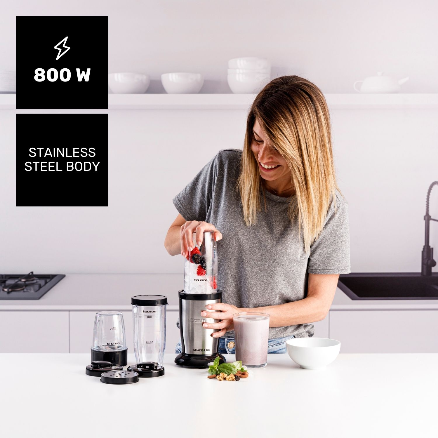Mujer prepara batido en licuadora con bayas y hielo. Vasos y bol sobre la mesa.